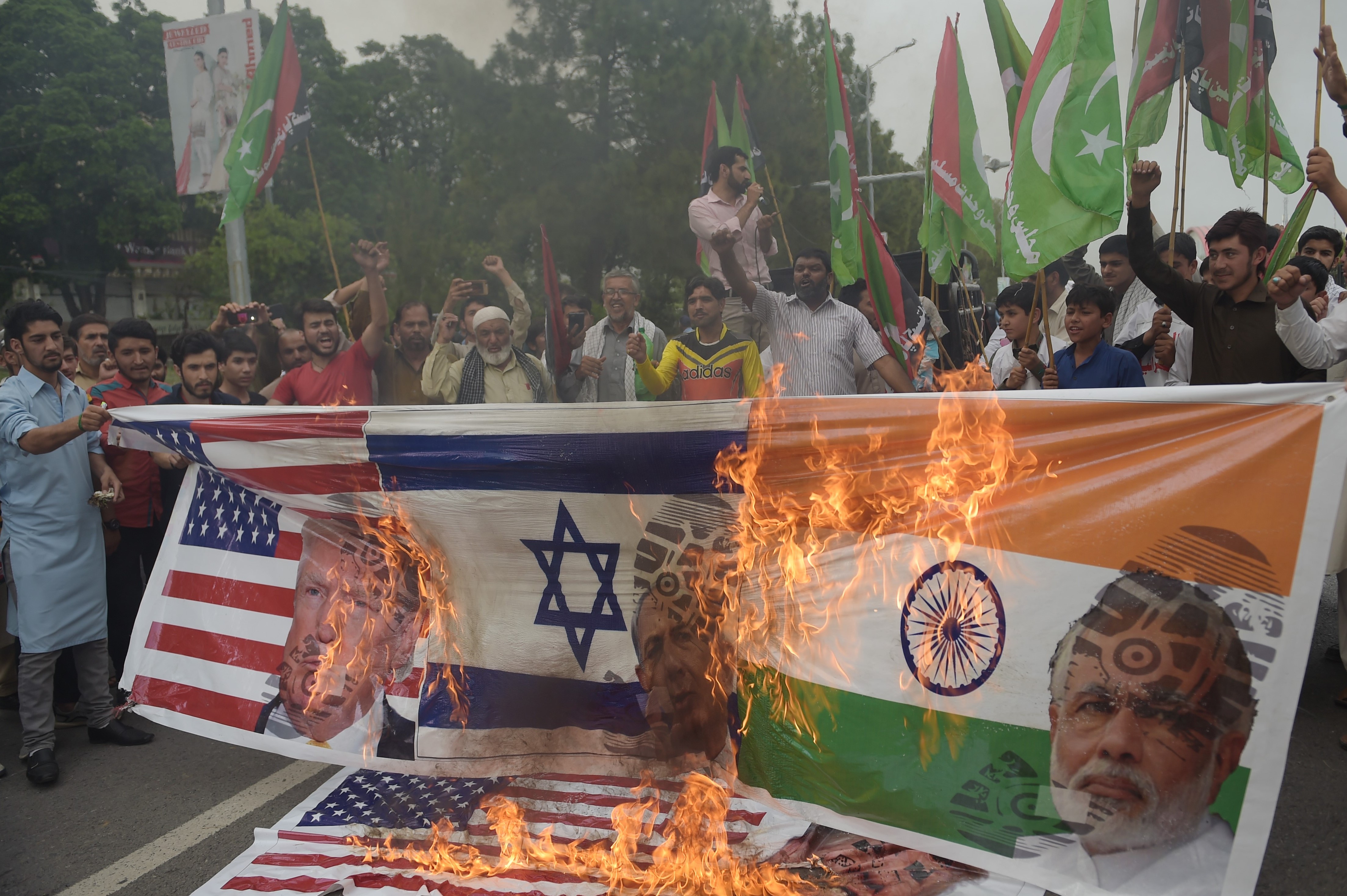 Pakistani activists burn a banner bearing the images of Modi, Netanyahu and Trump during a protest against the opening of the American embassy in Jerusalem in Islamabad on 13 May, 2018 (AFP)