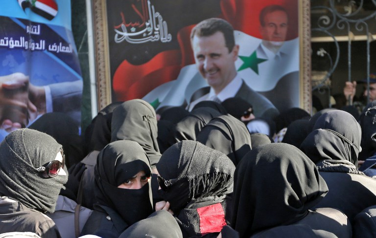 Syrians walk past a portrait of President Bashar al-Assad in Douma on 13 May (AFP)