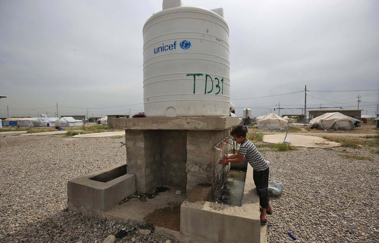 A boy washes his hands with water from a cistern at Laylan camp for the displaced, about 25 kilometres east of the northern multi-ethnic Iraqi city of Kirkuk, on 9 May 2019 (AFP)