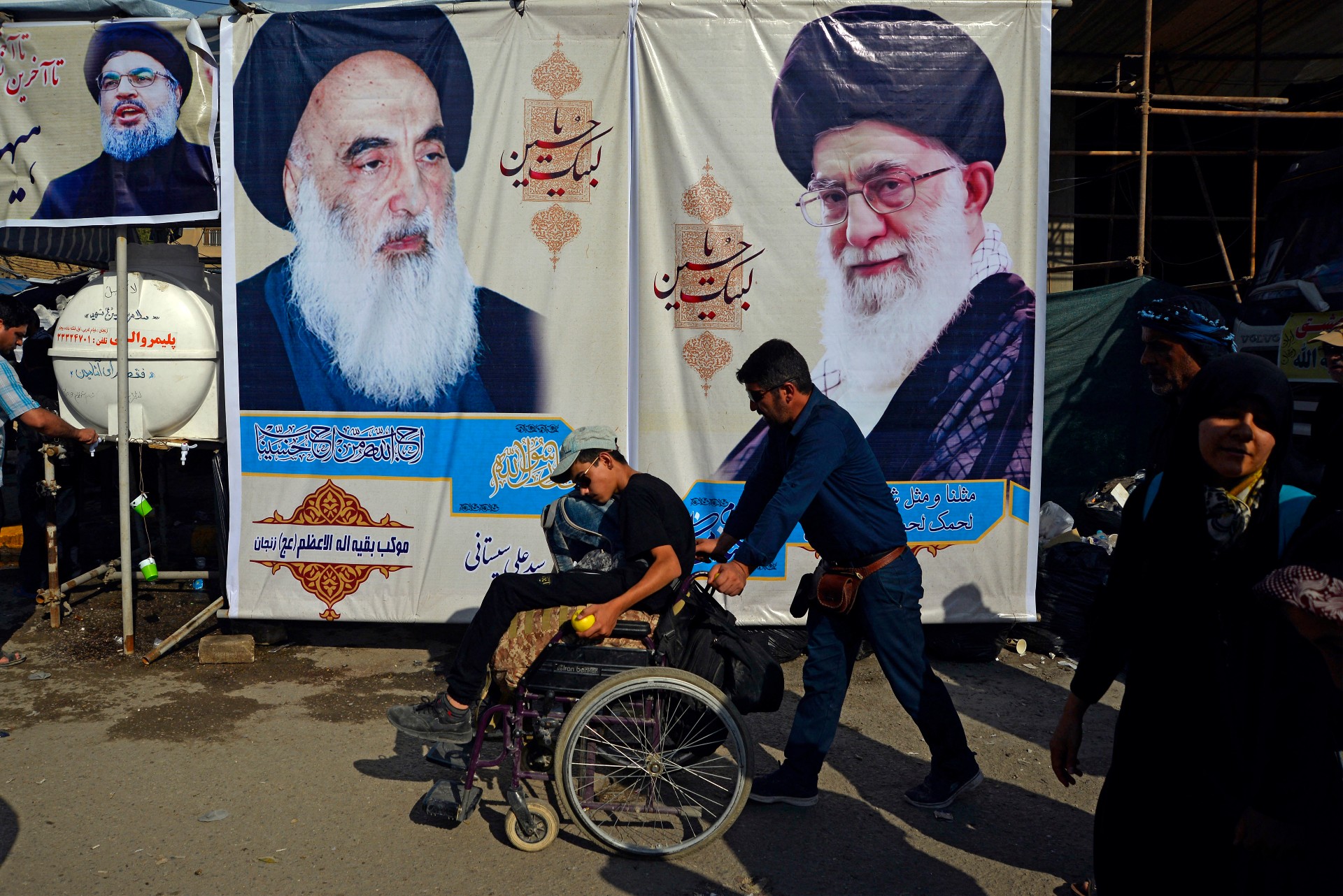 Shia pilgrims walk in front of posters of (R to L) Iran's Supreme Leader Ali Khamenei, Grand Ayatollah Ali Sistani, and Hezbollah leader Hassan Nasrallah (AFP)