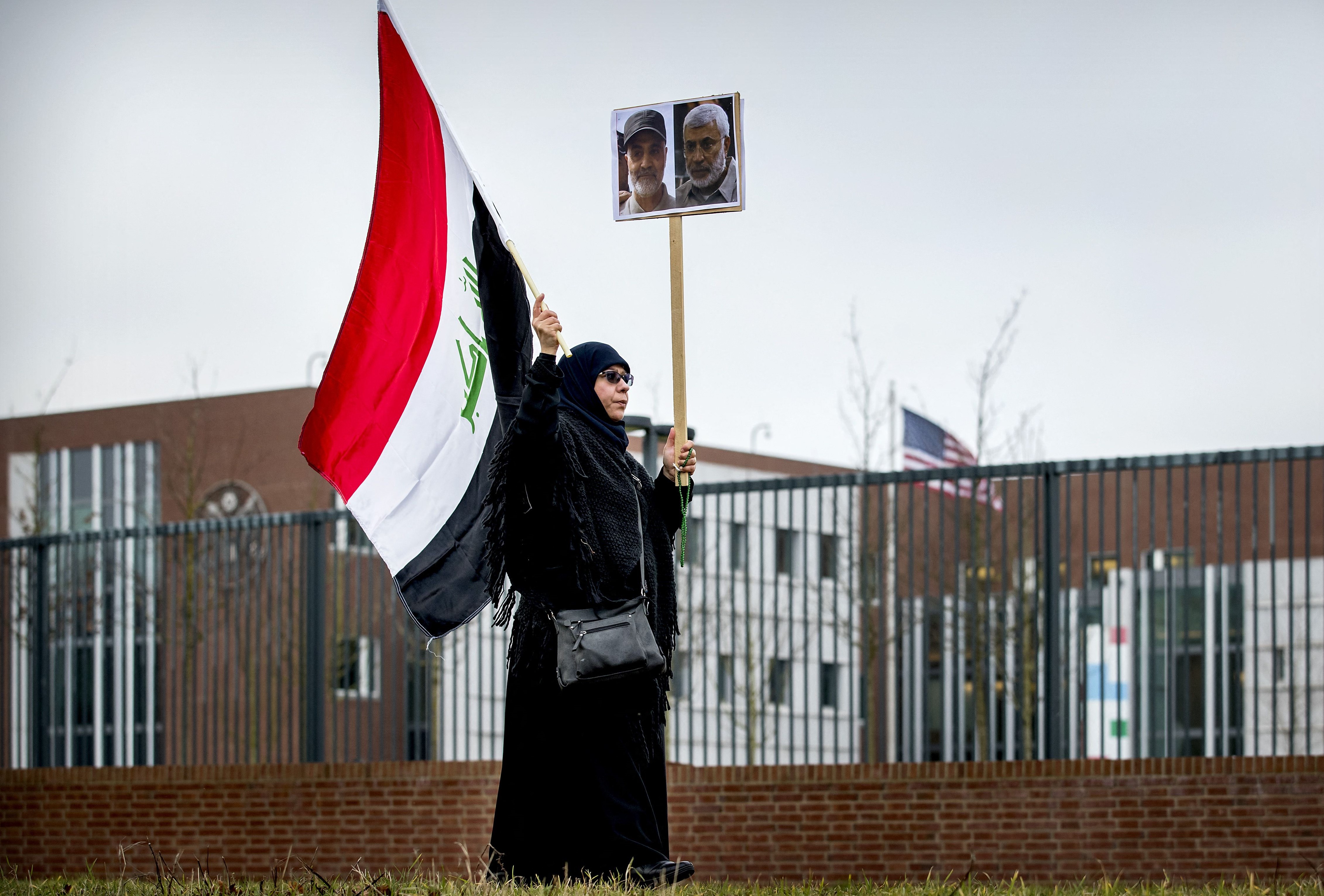 A protester holds an Iraqi flag and portraits of Iranian commander Qasem Soleimani (L) and Iraq's Hashed al-Shaabi military network deputy chief Abu Mahdi al-Muhandis, both killed in Baghdad early on January 3, 2020, by a US airstrike, as she protests outside the US Embassy in The Hague on January 7, 2020