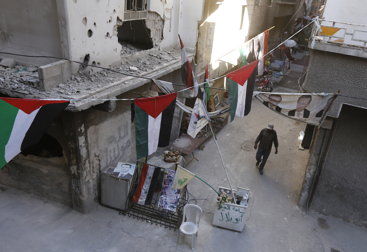 A man walks past destroyed buildings decorated with Palestinian flags in the Palestinian camp of Yarmuk southern Damascus (AFP)