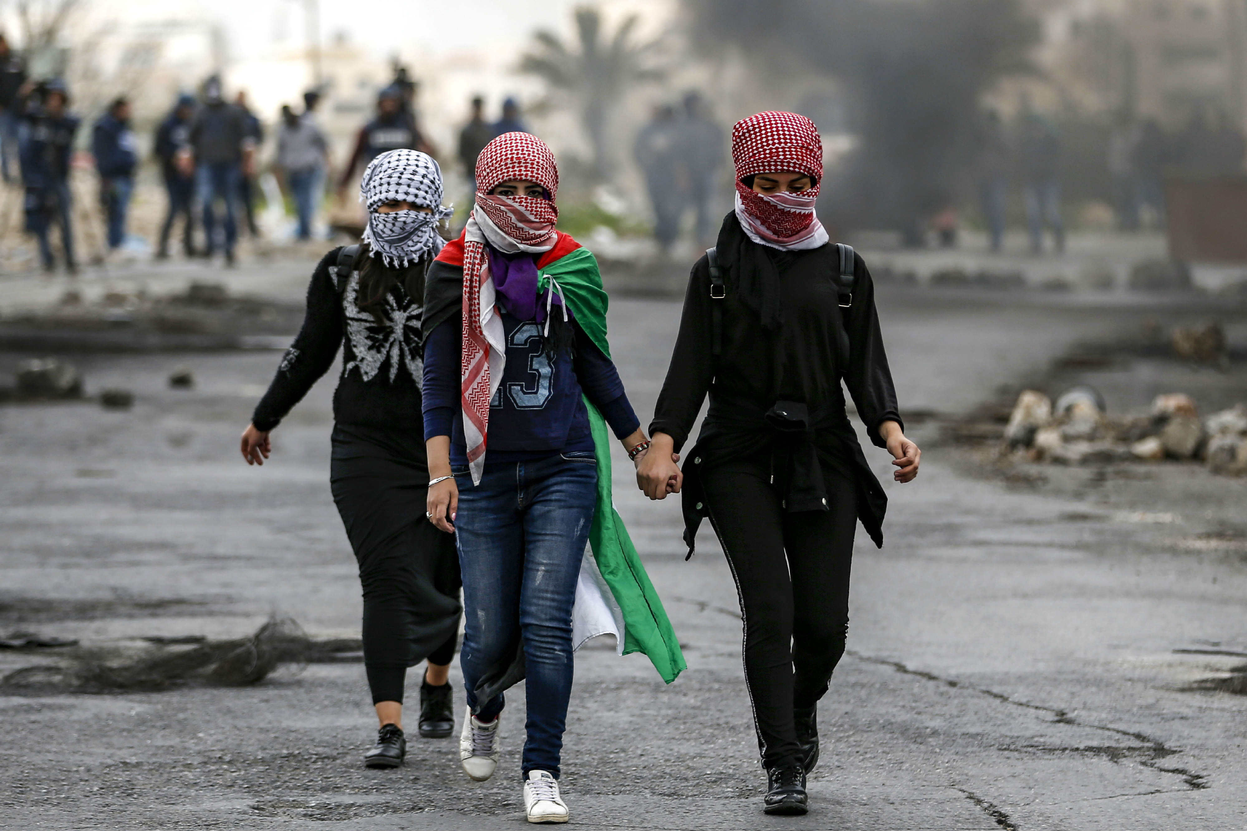 Palestinian girls with their faces covered with traditional chequered keffiyehs walk during clashes with Israeli forces following a demonstration marking Land Day in the West Bank (AFP)