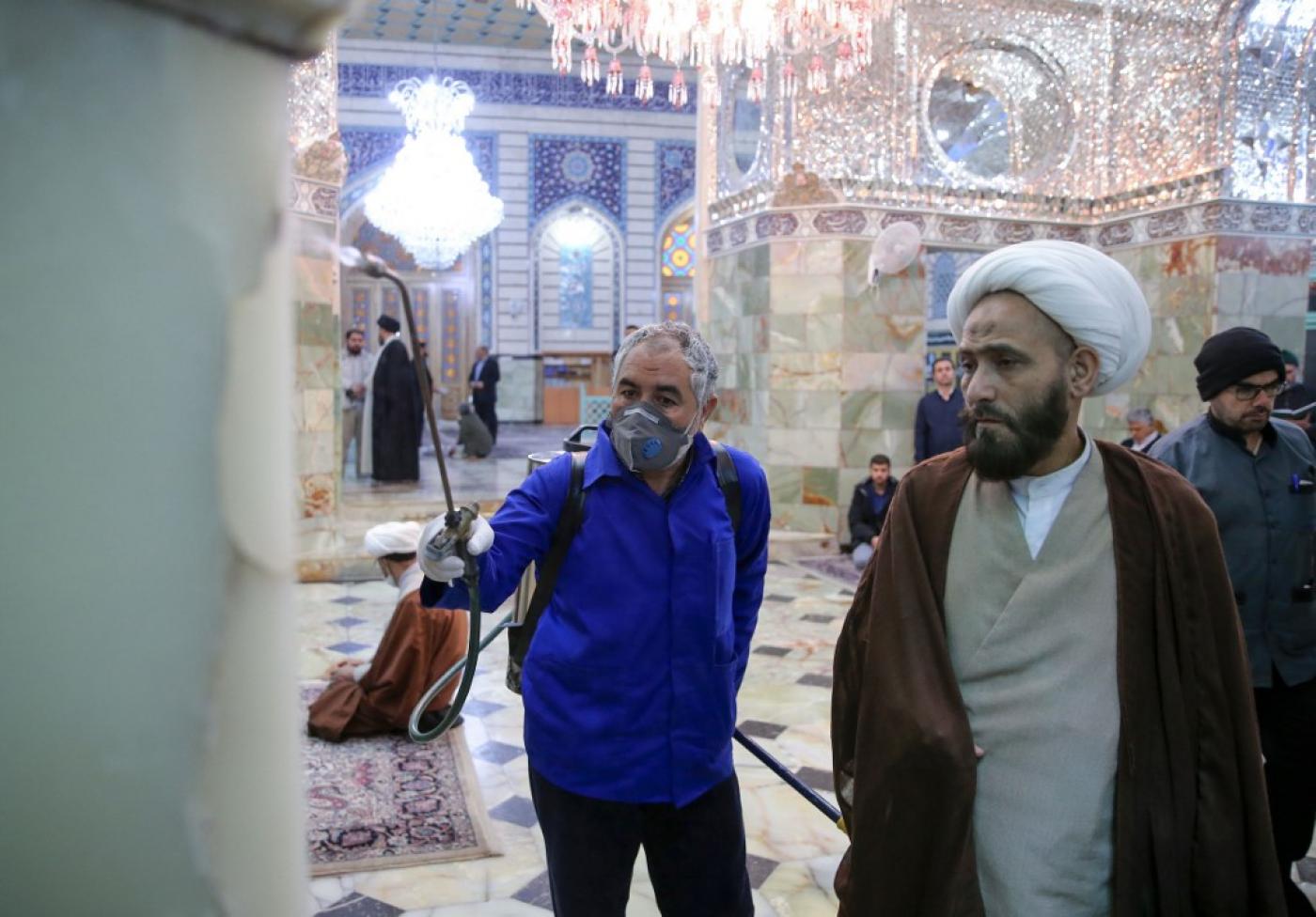 Un chiite iranien regarde un agent d’entretien désinfecter le sanctuaire de Fatima Masoumeh à Qom, le 25 février 2020, pour empêcher la propagation du coronavirus (AFP)