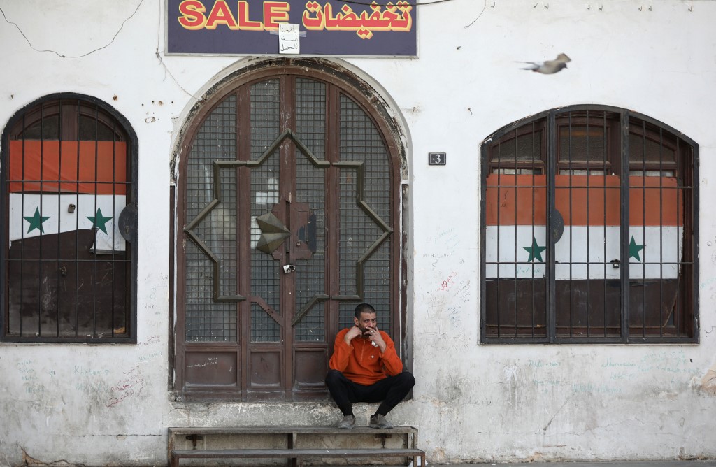 Un Syrien est assis devant un magasin fermé en raison du coronavirus, le 24 mars 2020 à Damas (AFP)