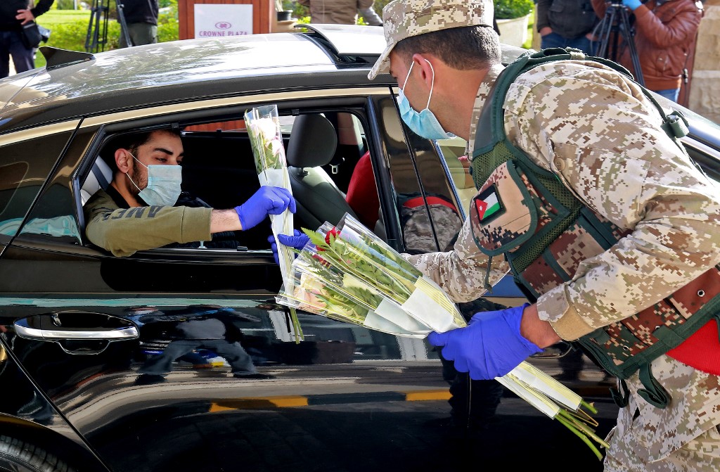 Un soldat jordanien offre des fleurs aux touristes et Jordaniens de retour de l’étranger mis en quarantaine dans une station balnéaire de la mer Morte, le 30 mars 2020 (AFP)