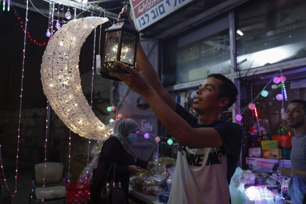 Un jeune Palestinien accroche des lumières décoratives et des lanternes dans un magasin de Jérusalem-Est, le 21 avril 2020, peu avant le début du Ramadan (AFP)