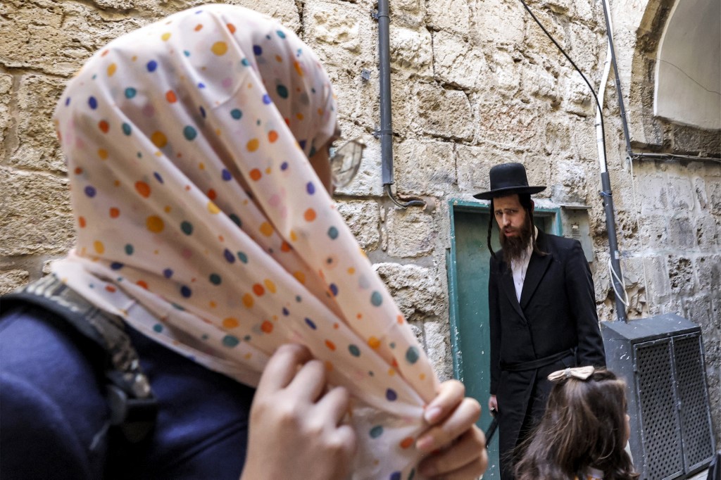 A Palestinian woman adjusts her headdress while an ultra-Orthodox Jewish man walks by in the Old City of Jerusalem on 28 March 2022. (Afp)