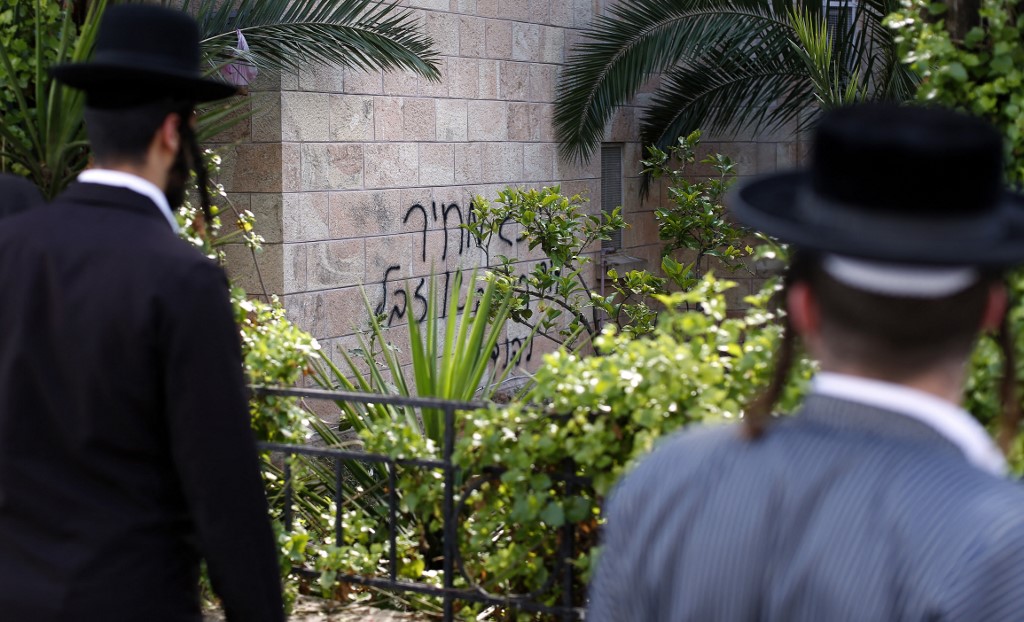 Deux juifs ultra-orthodoxes regardent des graffitis sur le mur d’une église indiquant en hébreu « Le roi David, roi des juifs et Jésus est une poubelle », à Jérusalem. 
