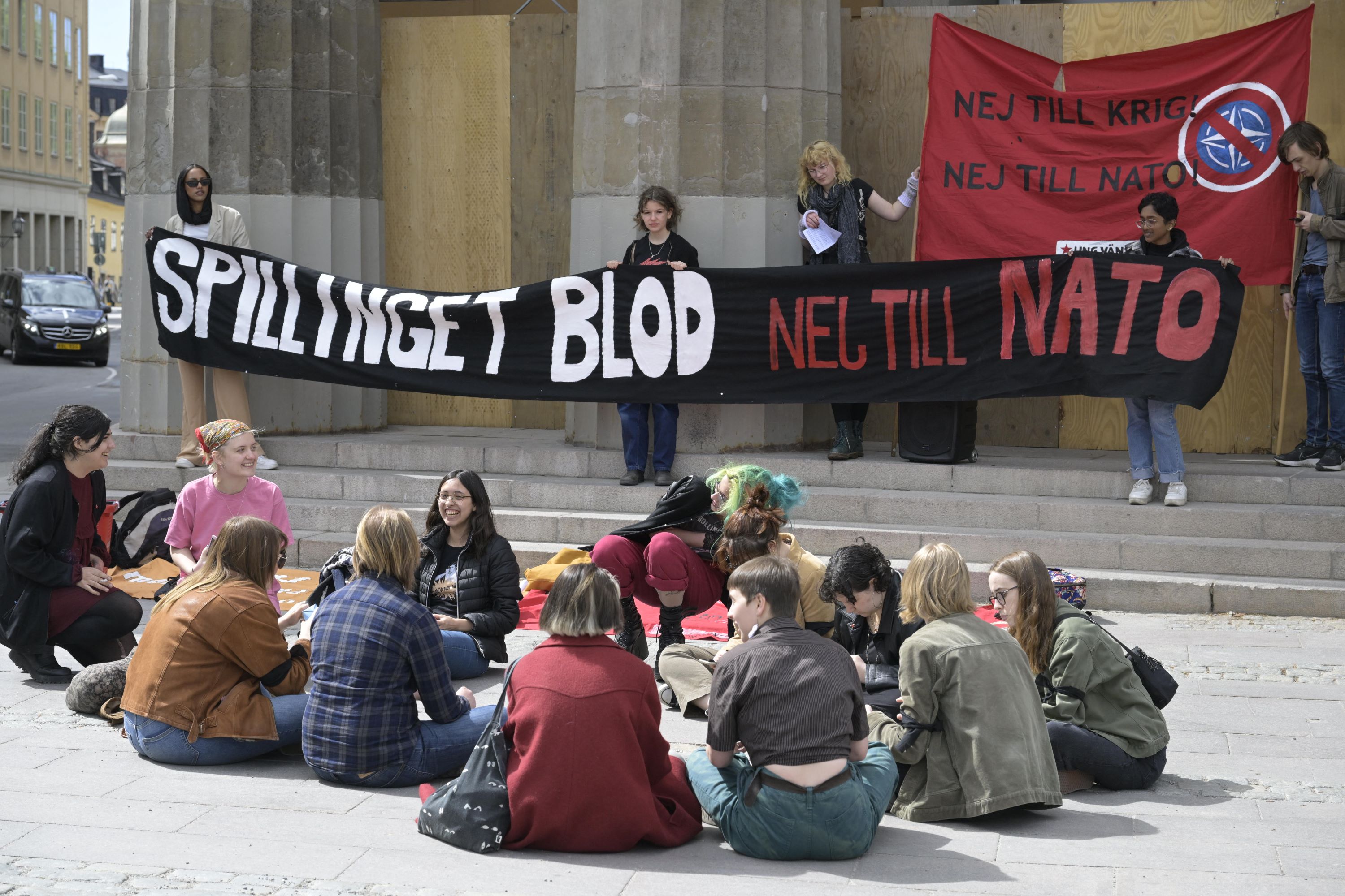 Demonstrators hold a banner to protest against Swedish membership's bid to join NATO reading 'Spilled blood, No to NATO' outside the Swedish Parliment in Stockholm, Sweden, on May 16, 2022 (AFP)