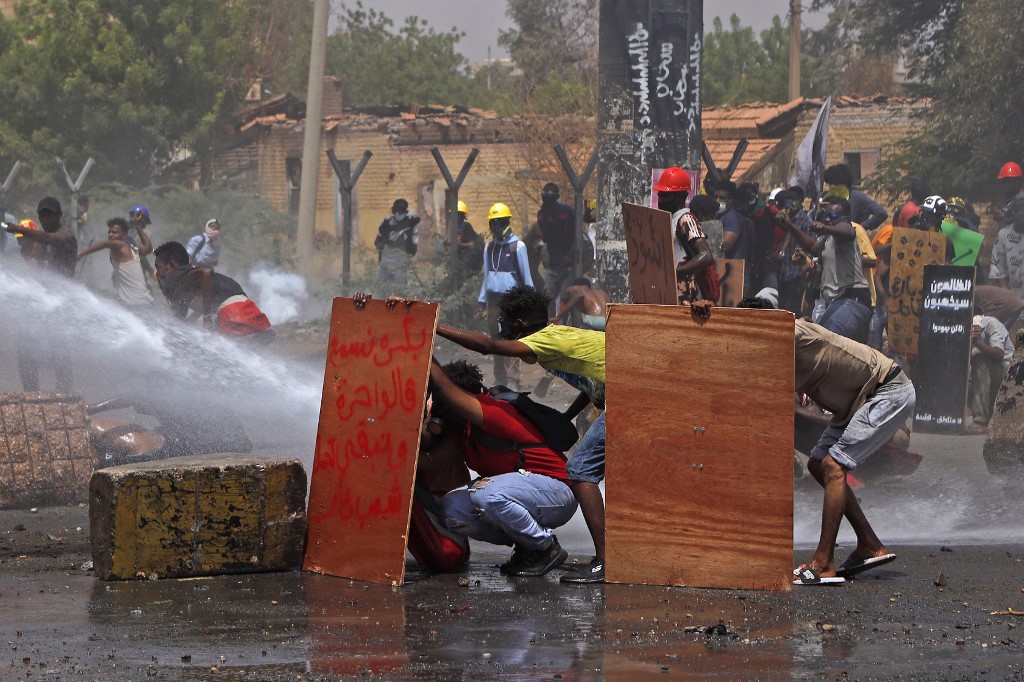 Anti-coup protesters take cover as riot police try to disperse them with water cannon during a demonstration against military rule in the centre of Sudan's capital Khartoum on June 30, 2022.