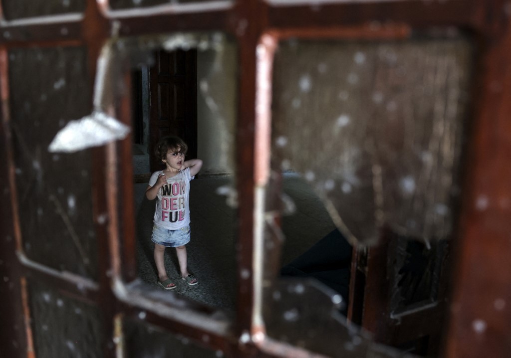 A Palestinian child stands behind a shattered window inside a building damaged following Israeli air strikes in Rafah in the southern Gaza Strip, on 7 August 2022 (AFP)