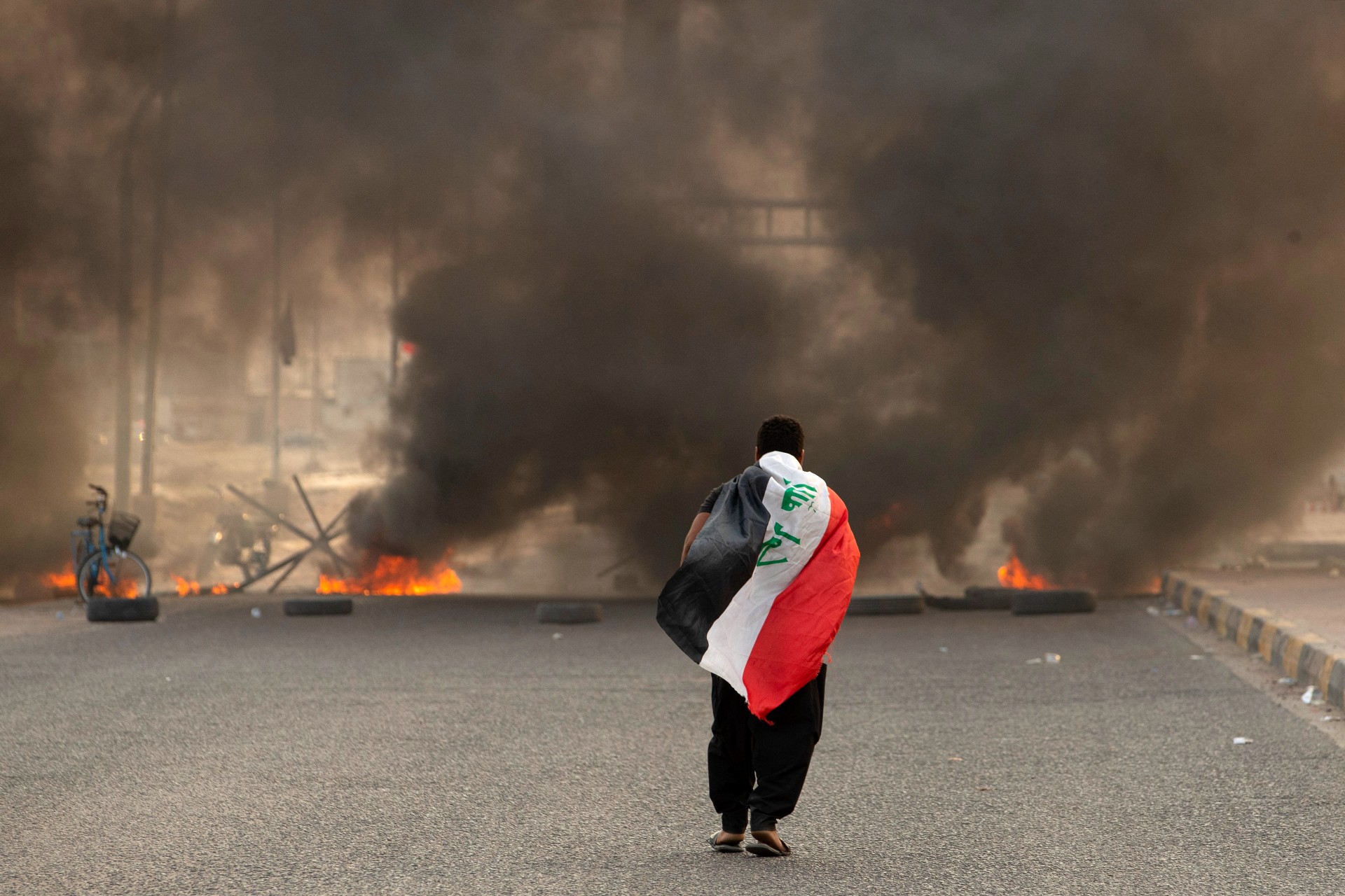 A Sadrist carries the Iraqi flag as he walks down a road blocked by burning tyres in Basra (AFP)