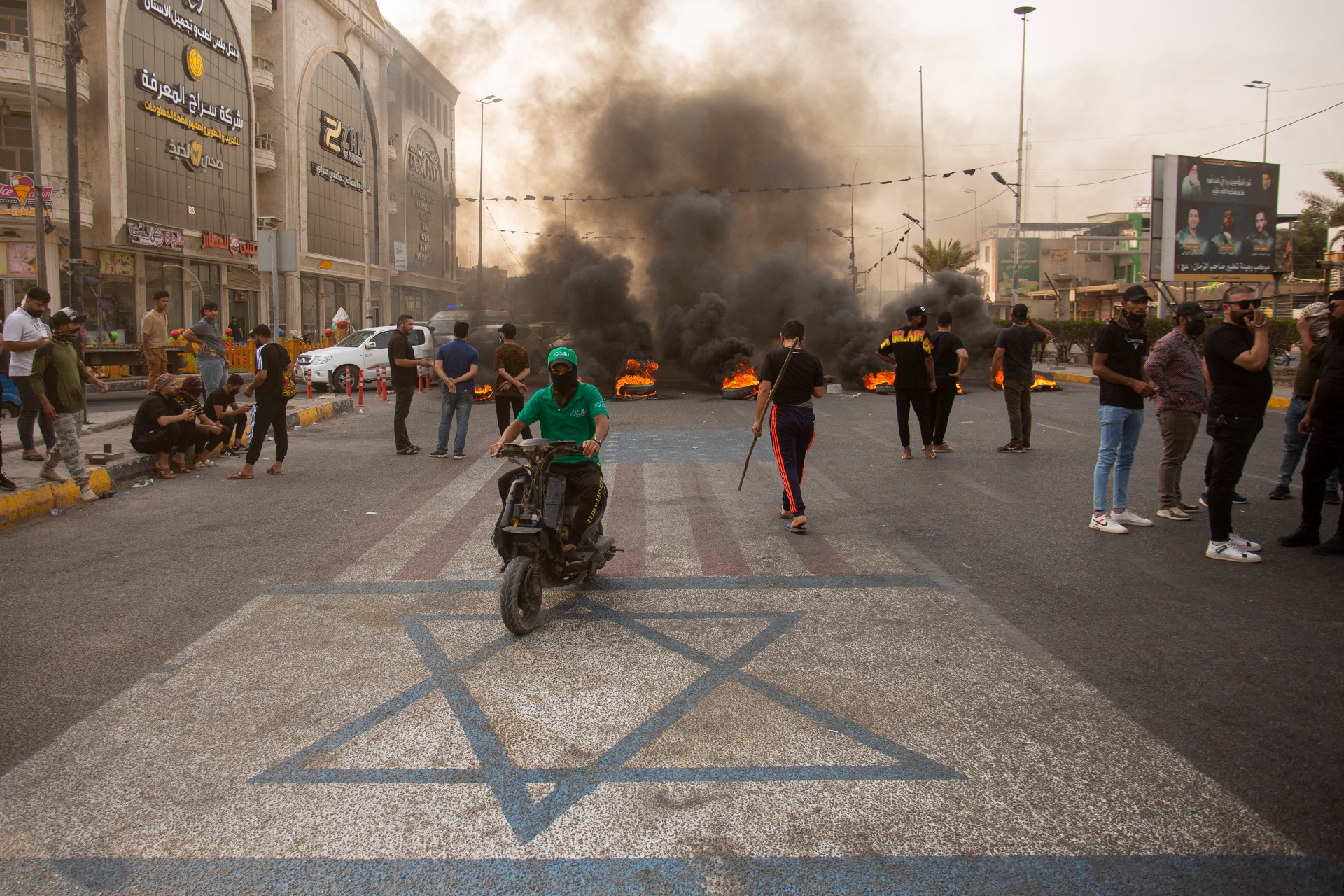 Sadr supporters walk on US and Israel flags, on a road blocked with burning tyres in Basra (AFP)