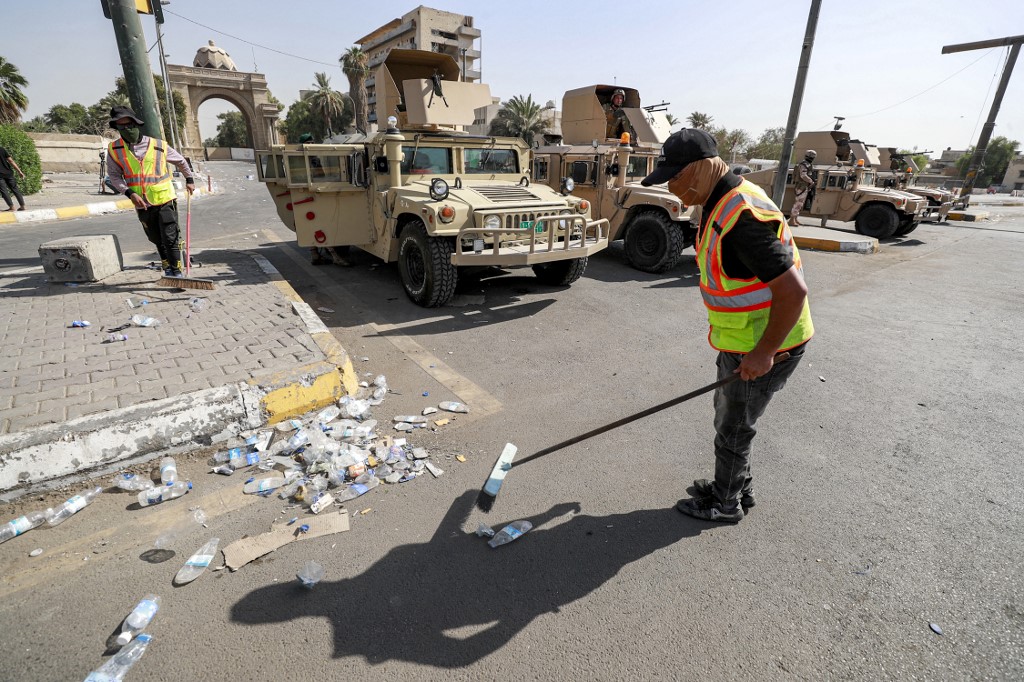 Municipality workers clean up while Iraqi army soldiers deploy to guard the entrance of the Green Zone in Baghdad on 30 August 2022 after the withdrawal of Sadr supporters (AFP)