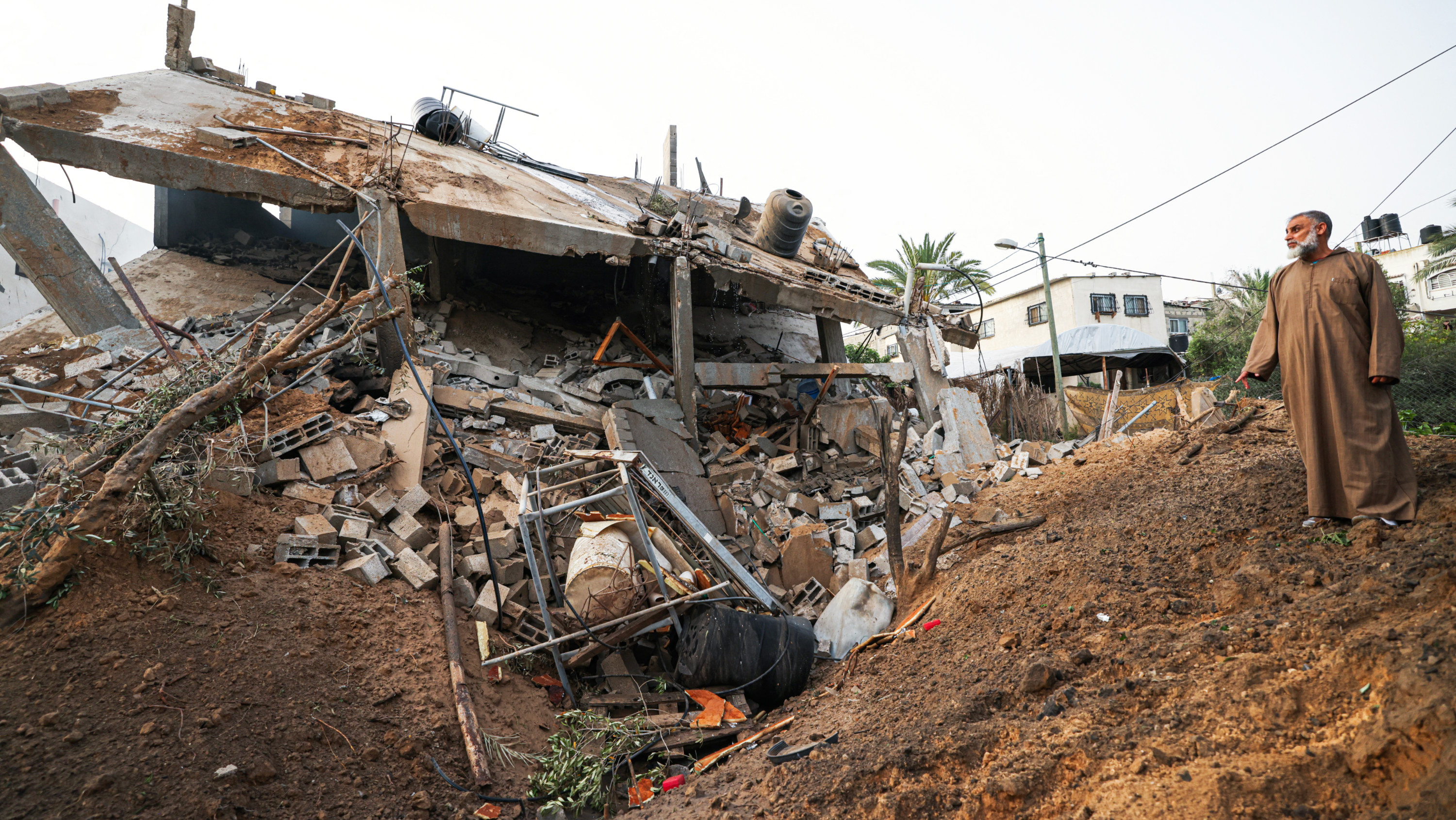 A Palestinian man looks at the rubble of a building following an Israeli air strike in Deir el-Balah, central Gaza Strip, on 12 May 2023 (AFP)