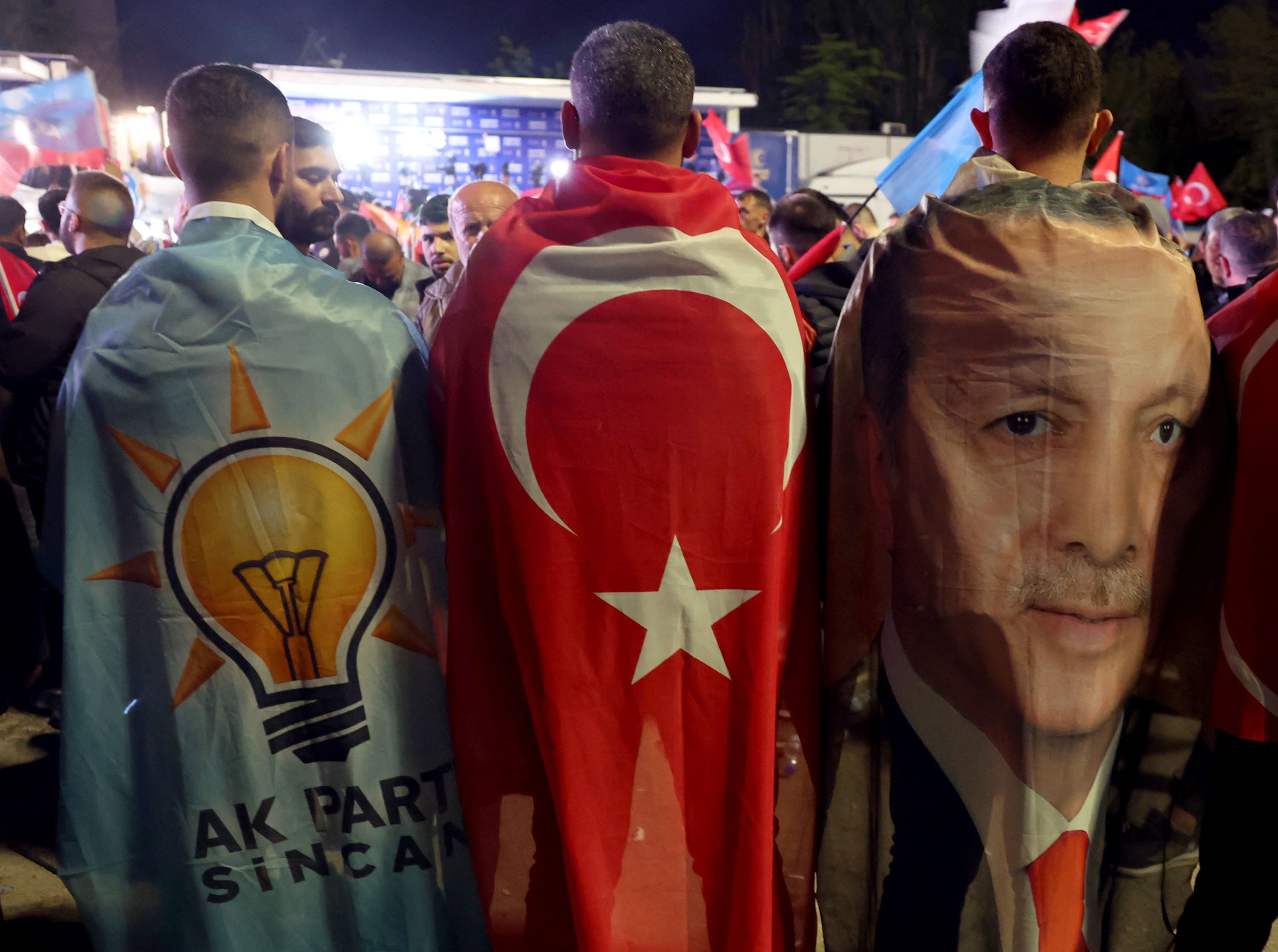Supporters drapped in the flags of the AK Party, Turkish Flag and image of Turkish President Tayyip Erdogan stand outside the AK Party headquarters after polls closed in Turkey (AFP)