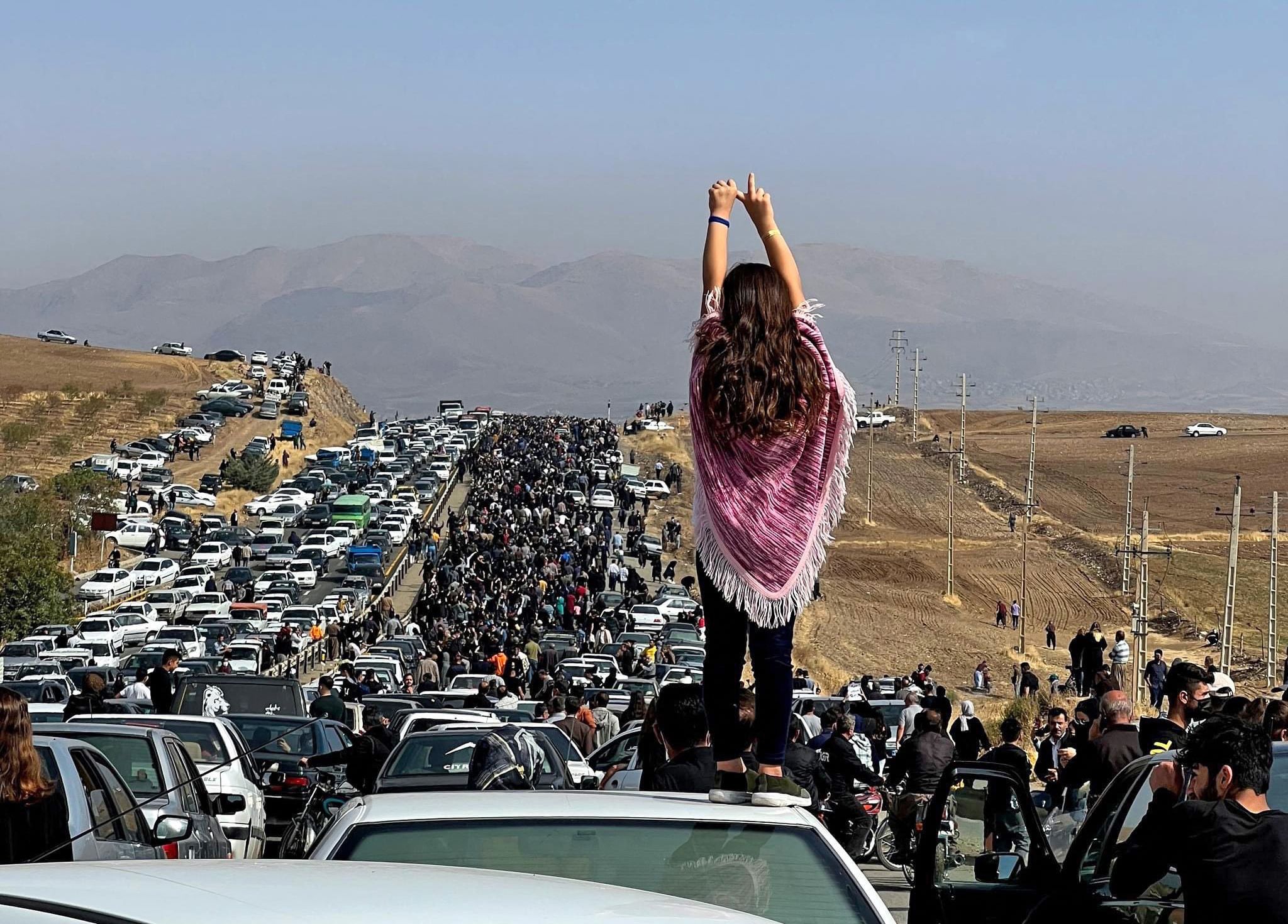 Image posted on Twitter reportedly on October 26, 2022 shows an unveiled woman standing on top of a vehicle as thousands make their way towards Aichi cemetery in Saqez, Mahsa Amini's home (Reuters)