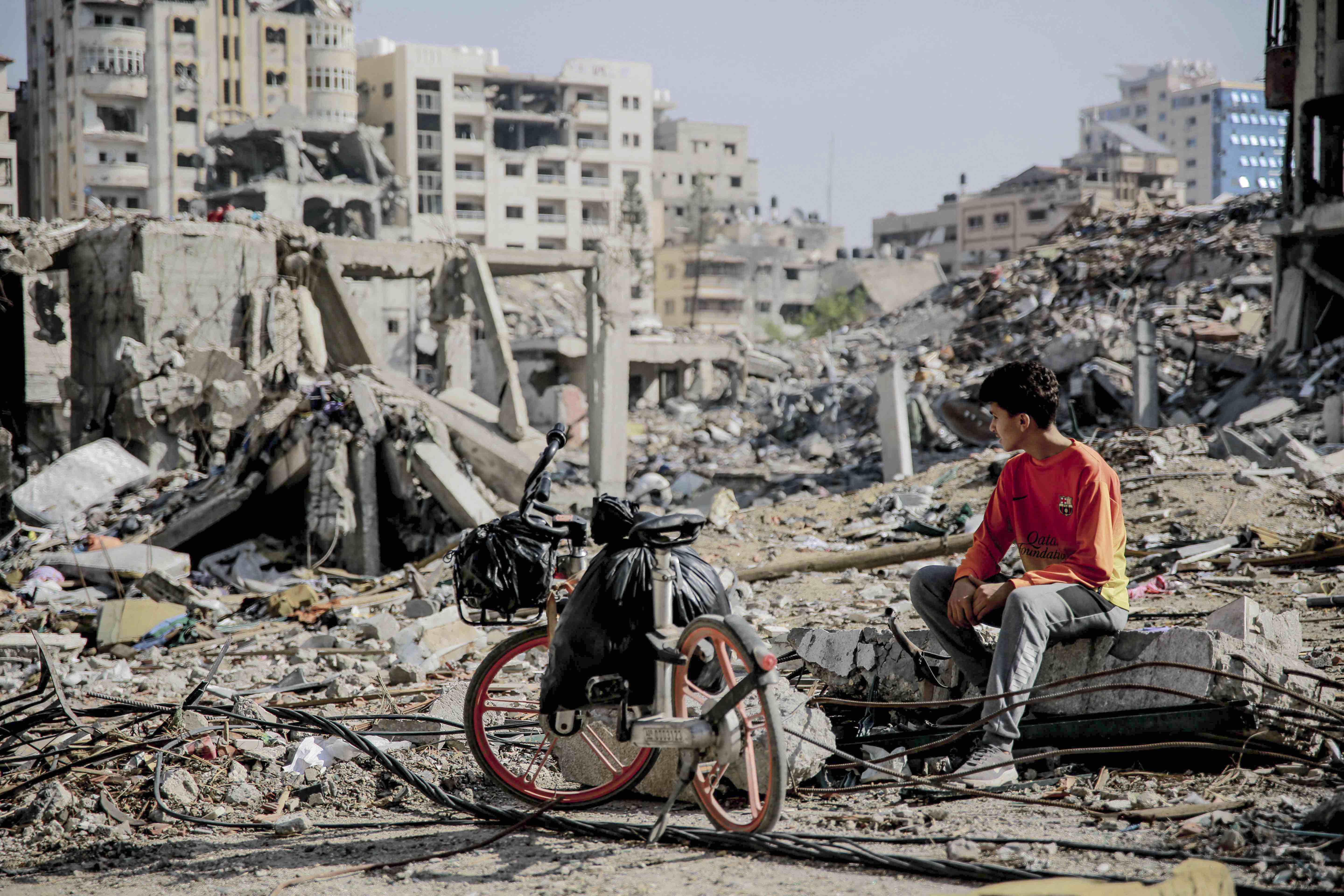 A Palestinian youth sits next to his bicycle amid the rubble of destroyed buildings in northern Gaza following weeks of Israeli bombardment, as a four-day truce took effect on 24 November 2023.