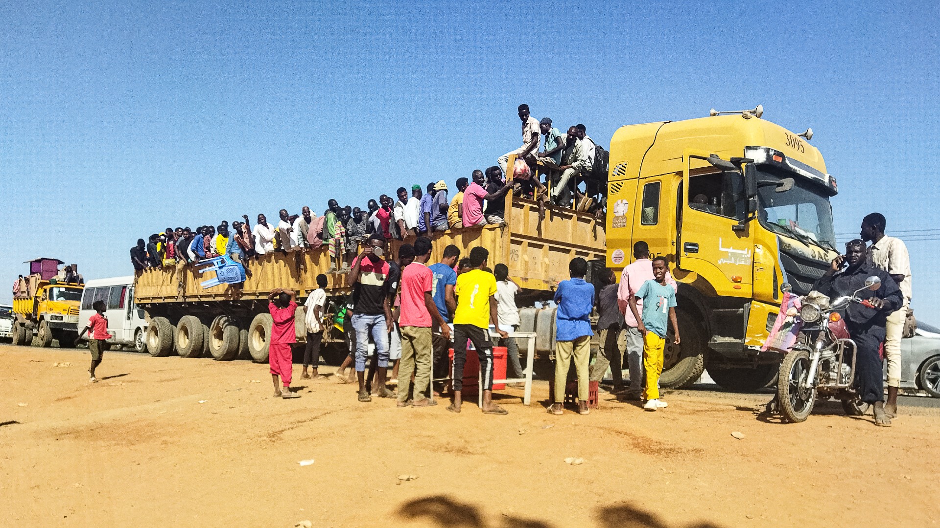 People displaced by the conflict in Sudan get on top of the back of a truck moving along a road in Wad Madani, 16 December (AFP)