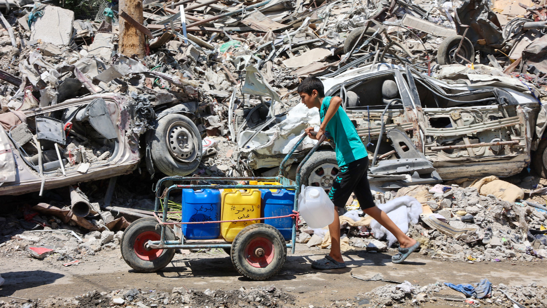 A boy pushes a cart filled with water containers amid the rubble of buildings destroyed during Israeli bombardment at the Jabalia camp for displaced Palestinians on 29 August (Omar al-Qattaa/AFP)