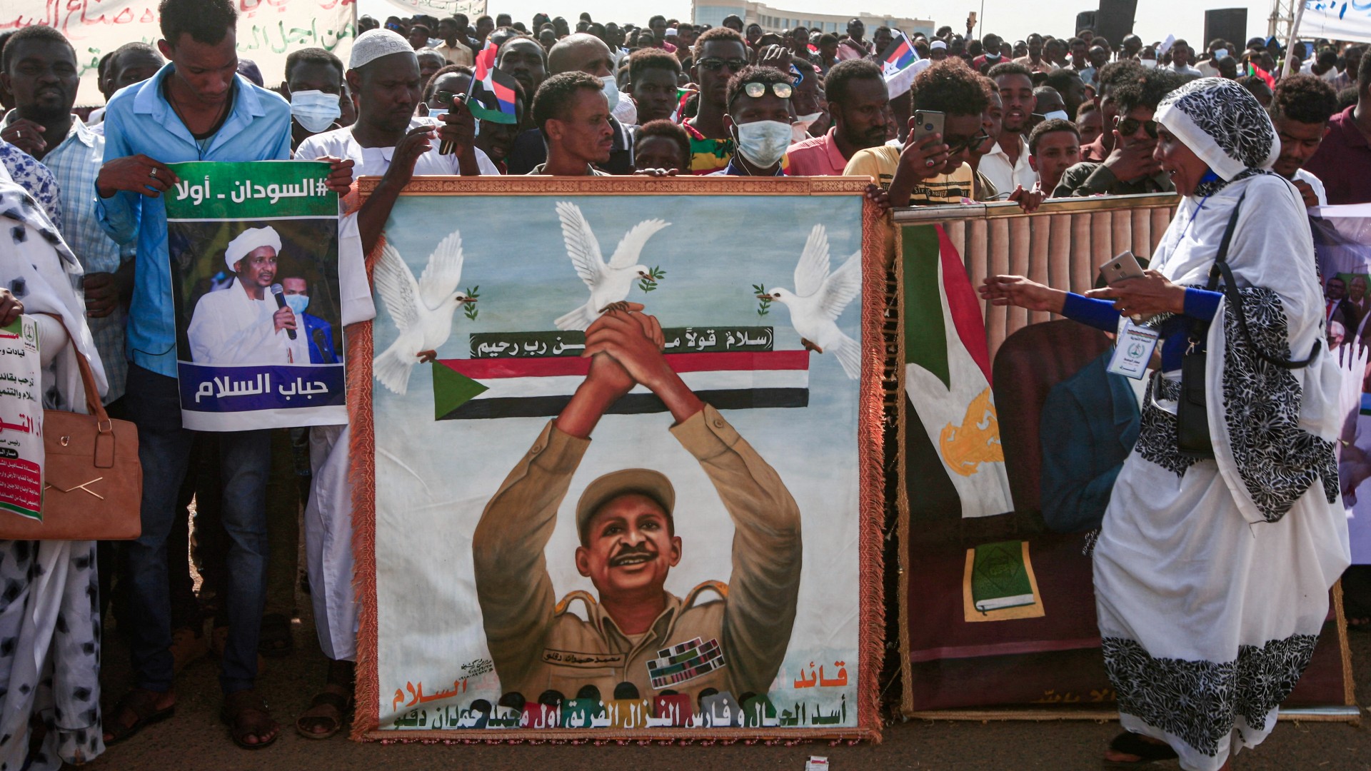 People stand holding signs showing Hemeti during a ceremony to sign a South Sudan peace accord in October 2020 (AFP)