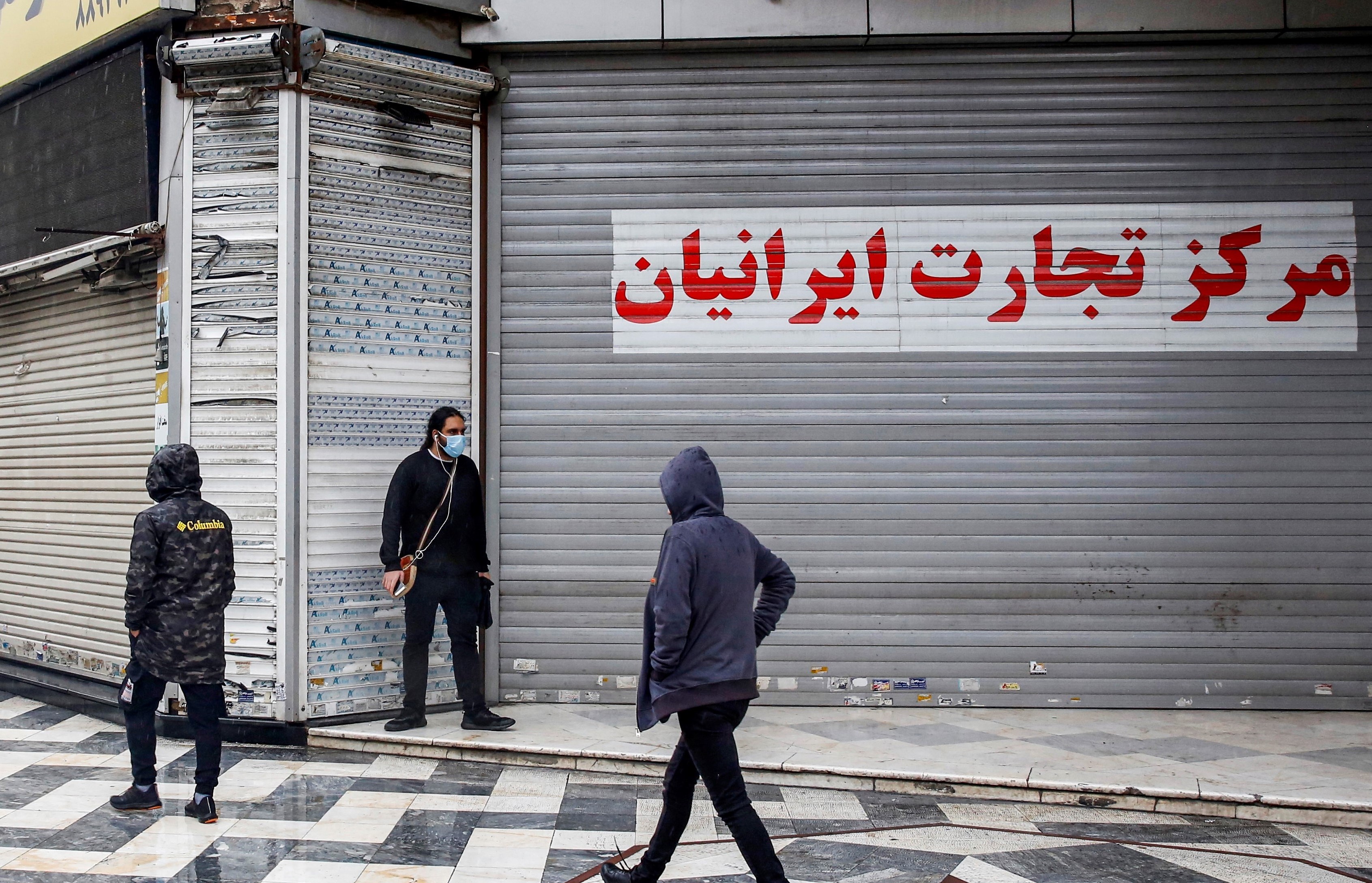 Pedestrians, mask-clad due to the COVID-19 coronavirus pandemic, walk past closed shops along a street in Iran's capital Tehran on November 21, 2020,