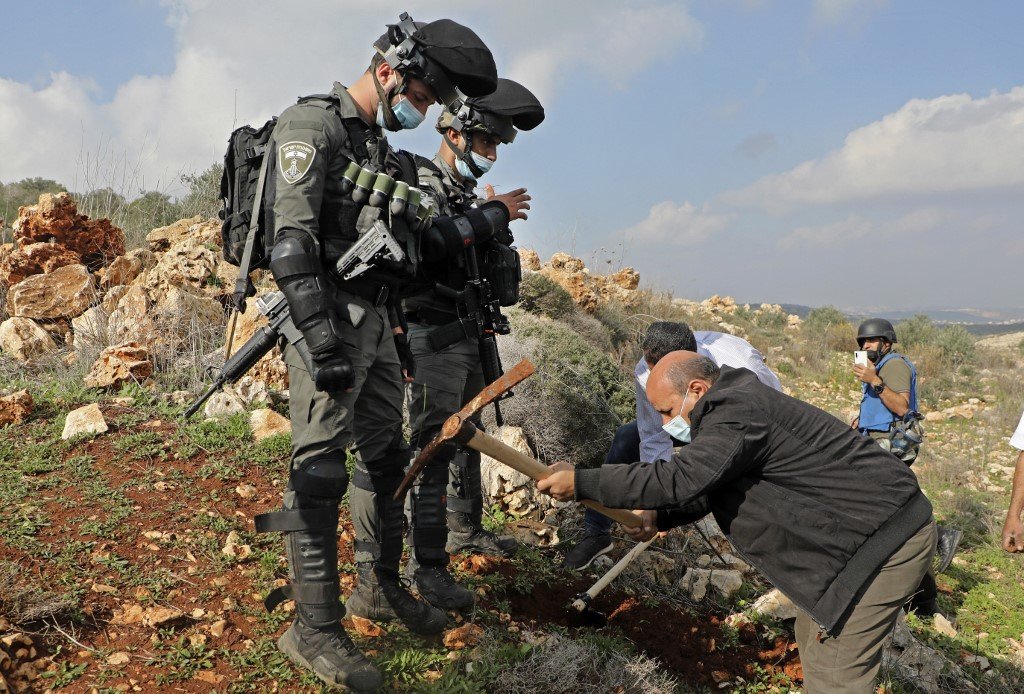Des soldats israéliens se tiennent devant des Palestiniens qui tentent de planter des oliviers sur des terres palestiniennes près de Salfit, en Cisjordanie occupée, le 22 décembre 2020 (AFP)