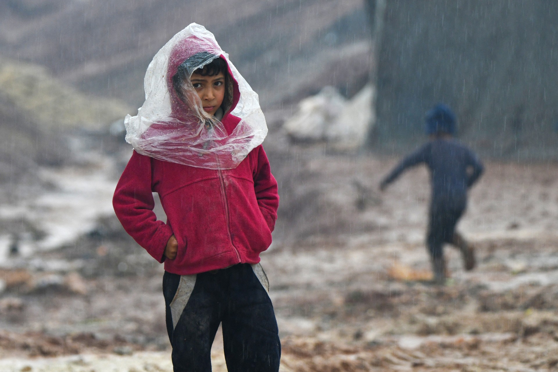 A child poses for a picture in the Atme camp for displaced Syrians close to the border with Turkey in Syria's northwestern Idlib province after heavy rains, on 17 January, 2021 (AFP)