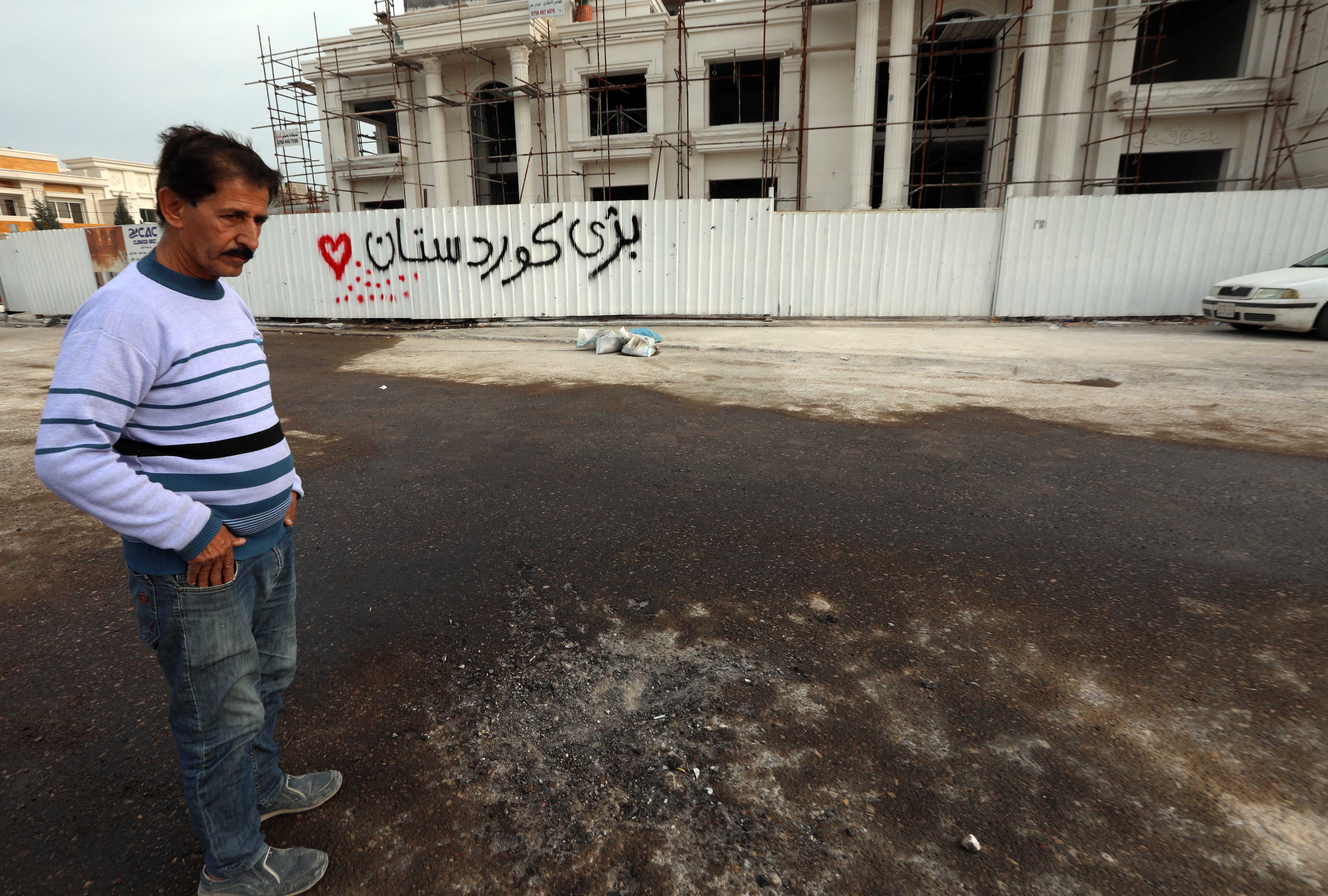 A man stands near a fence with graffiti reading in Kurdish "long live Kurdistan", at the scene of a rocket attack targeting Erbil the previous night (AFP)