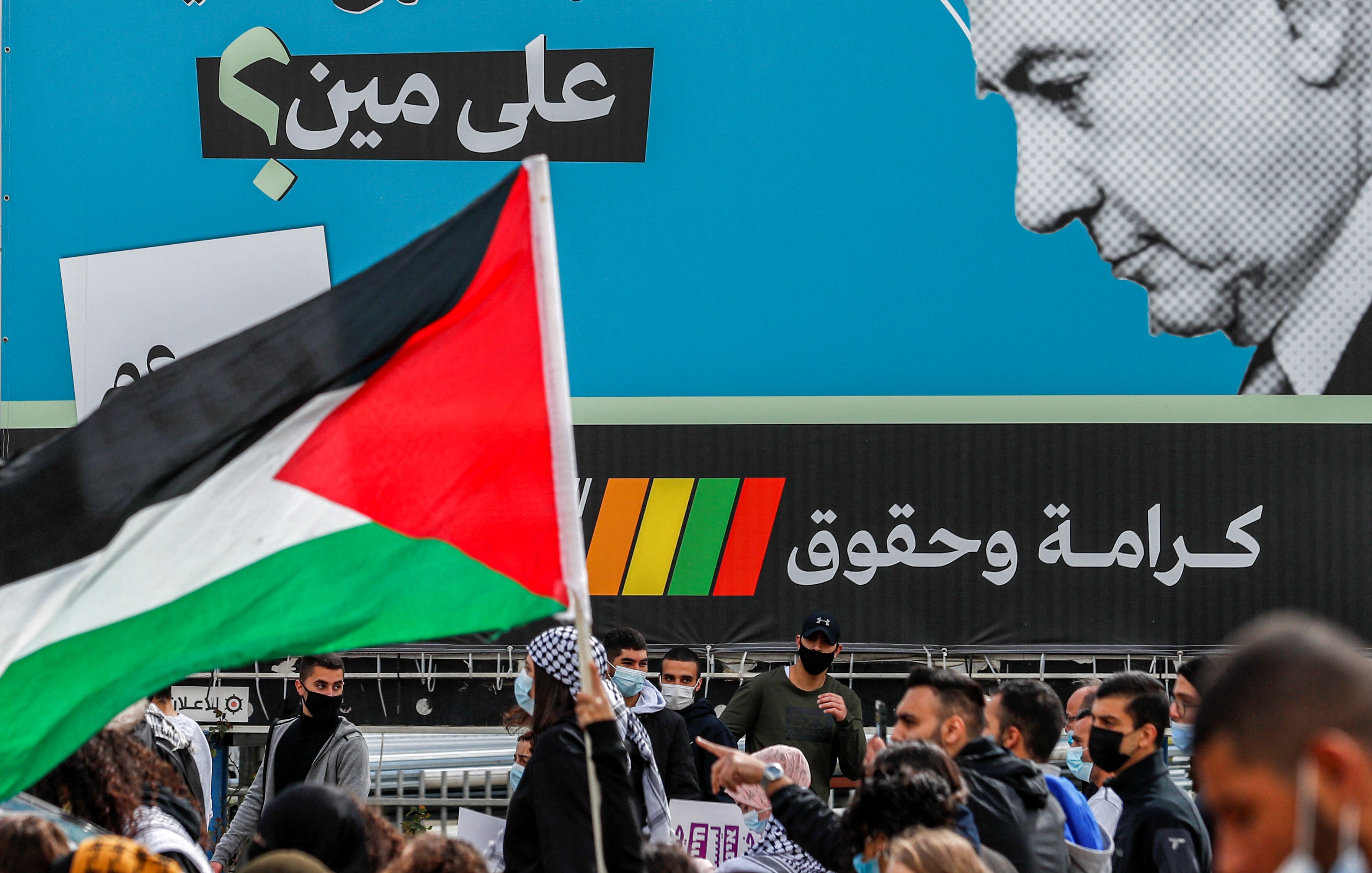 A demonstrator holds a Palestinian flag near an electoral billboard by the predominantly Arab Israeli electoral alliance the Joint List depicting Israeli prime minister Benjamin Netanyahu with a caption reading in Arabic "whom is he fooling?" during a demonstration