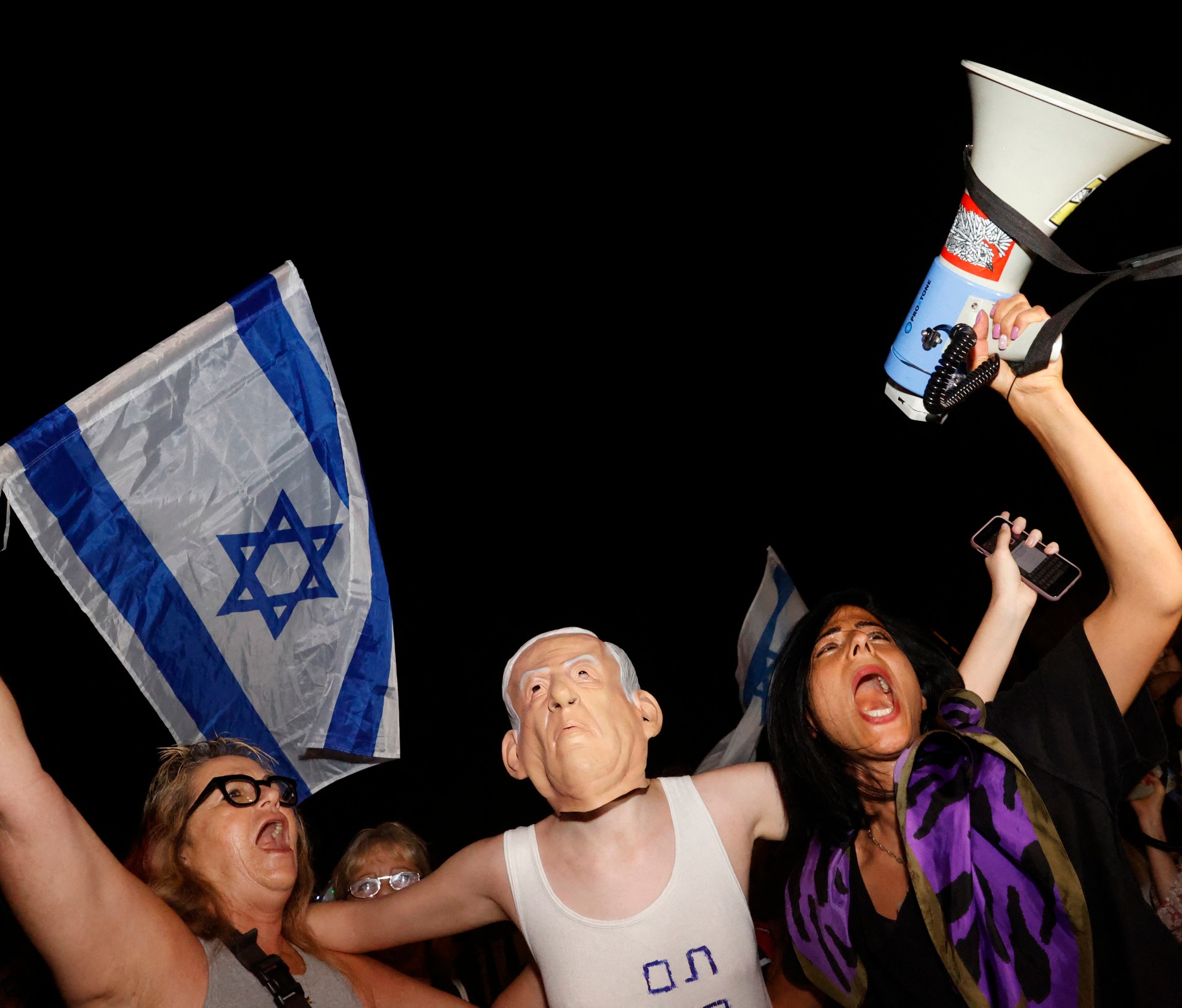An Israeli protester stands between others wearing a mask of Prime Minister Benjamin Netanyahu during a demonstration in support of the opposition for the formation of a government (AFP)