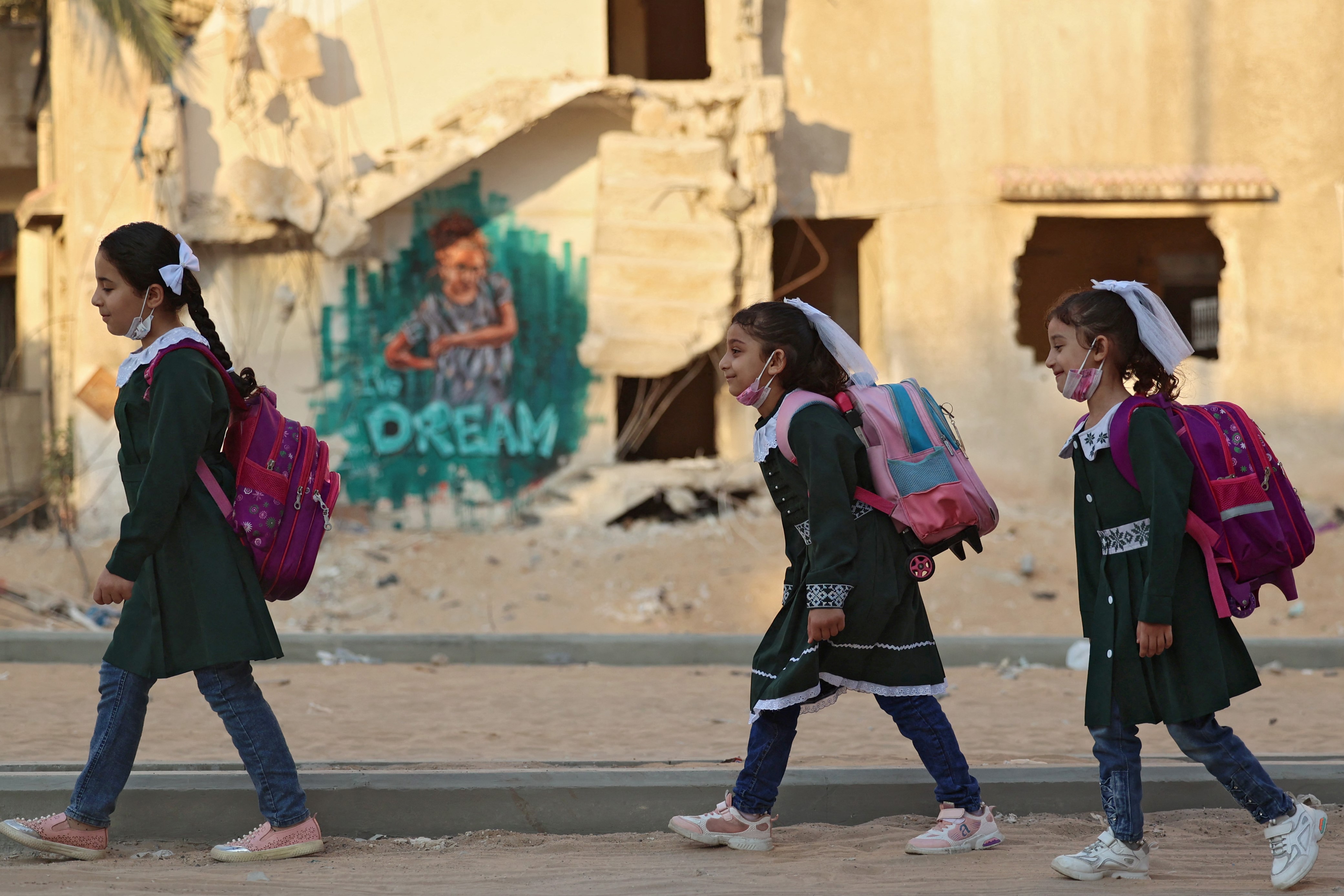 Palestinian children walk past a building, destroyed during the recent 11-day war between Israel and the Palestinian Hamas movement, on their way to school for the first day of the new scholastic year in Gaza City on August 16, 2021.