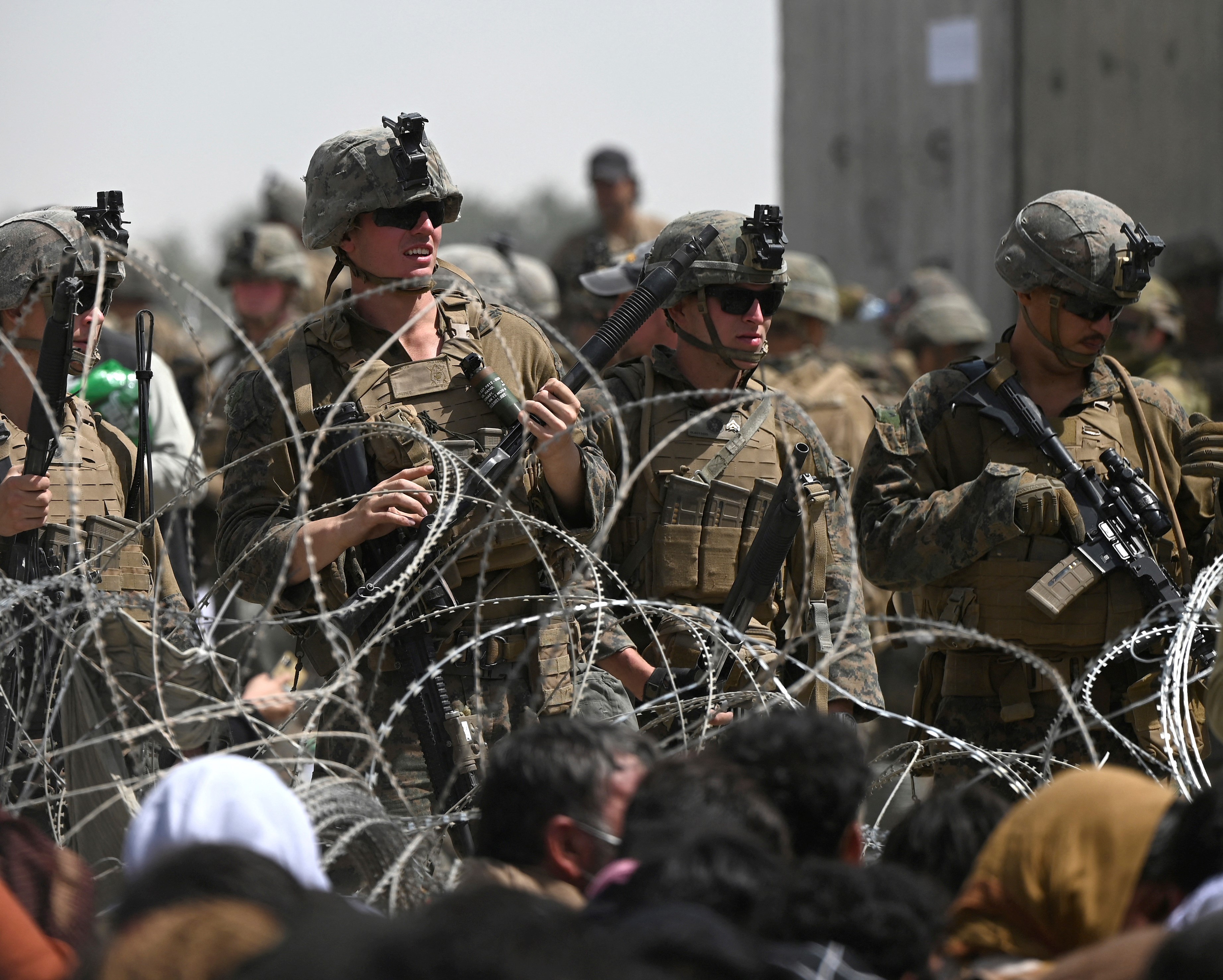 US soldiers stand guard behind barbed wire as Afghans sit on a roadside near the military part of the airport in Kabul on 20 August, 2021(AFP)