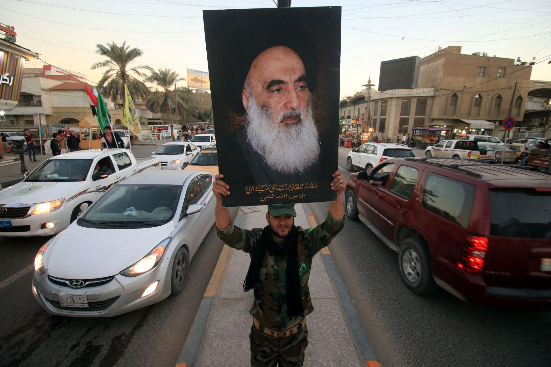 A member of the Hashed al-Shaabi (Popular Moblisation units) carries a portrait of Iraqi Shia cleric Grand Ayatollah Ali al-Sistani in a street in the southern city of Basra (AFP)