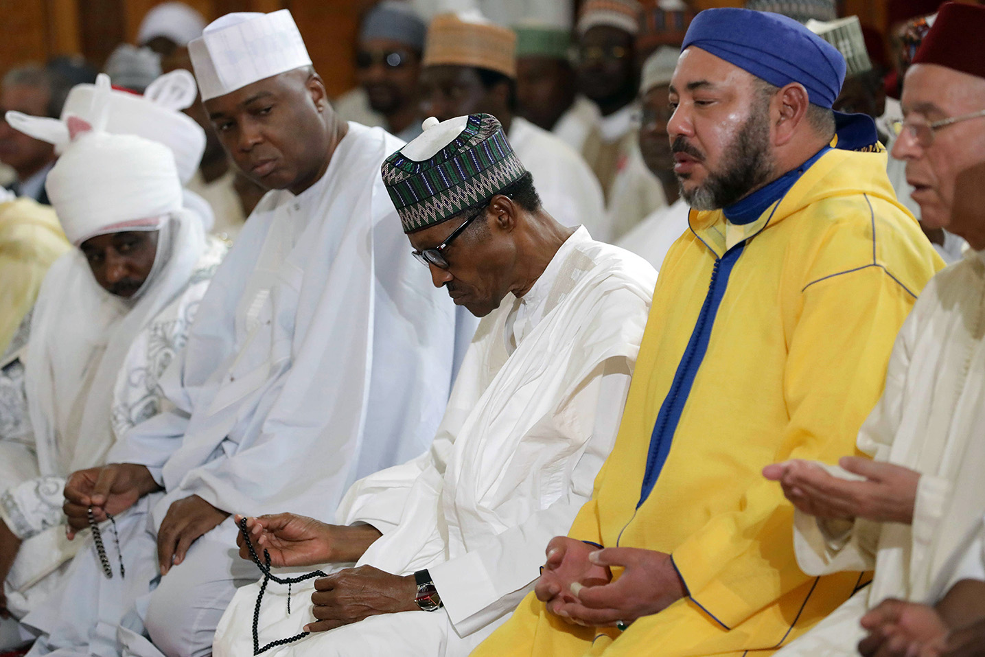 Le roi du Maroc Mohammed VI (en jaune), accompagné du président nigérian, Muhammadu Buhari (à gauche), prie dans la mosquée nationale nigériane à Abuja, le 2 décembre 2016 (AFP)