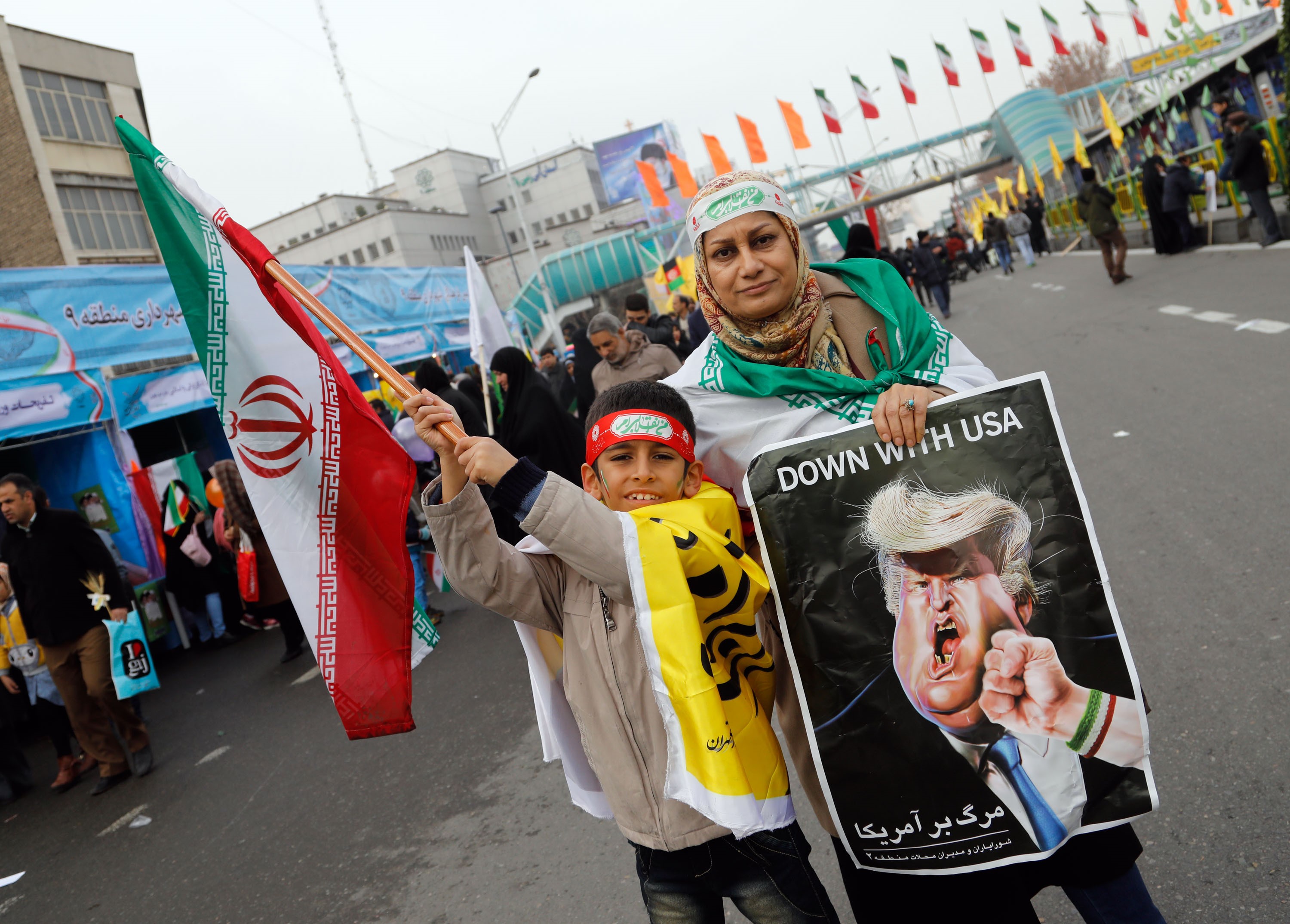 An Iranian woman holds a placard showing a caricature of US President Donald Trump being punched by a hand wearing a bracelet of the Iranian flag February, 2017 (AFP)