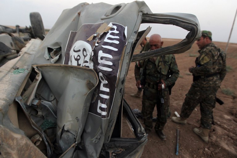 Peshmerga fighters inspect the remains of a car bearing the IS flag near Mosul in August 2014 (AFP)