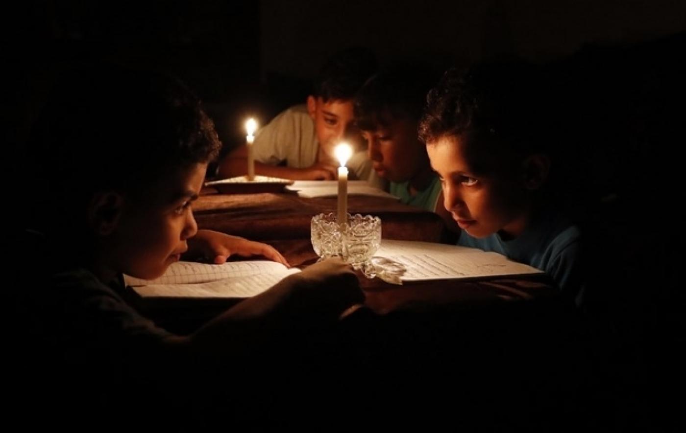 Des enfants palestiniens lisent des livres chez eux à la lueur de bougies en raison des pénuries d’électricité à Gaza, en juin 2017 (AFP)