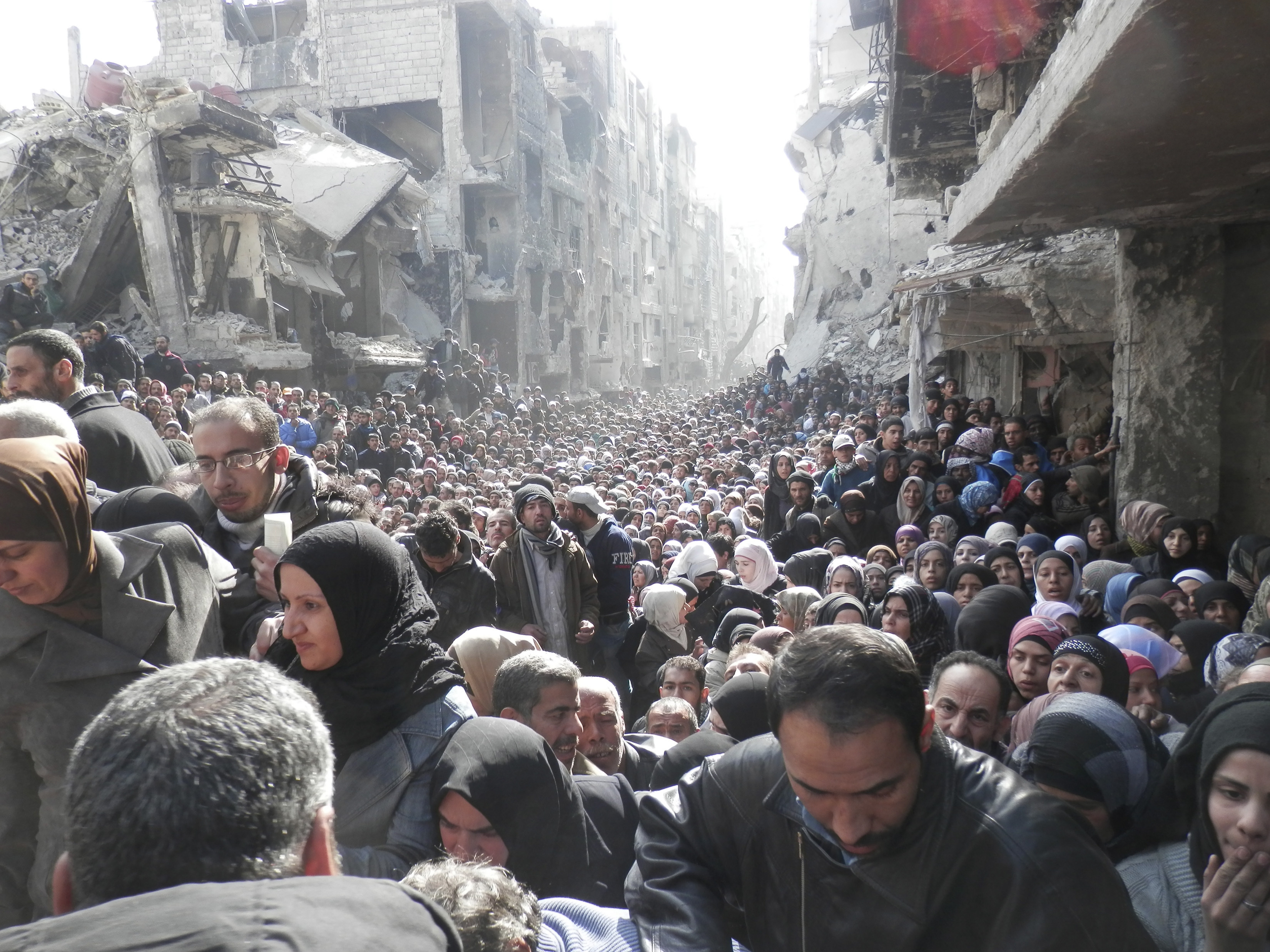 Residents wait to receive food aid distributed by UNRWA at the besieged Yarmouk camp, south of Damascus, in 2014 (Reuters)