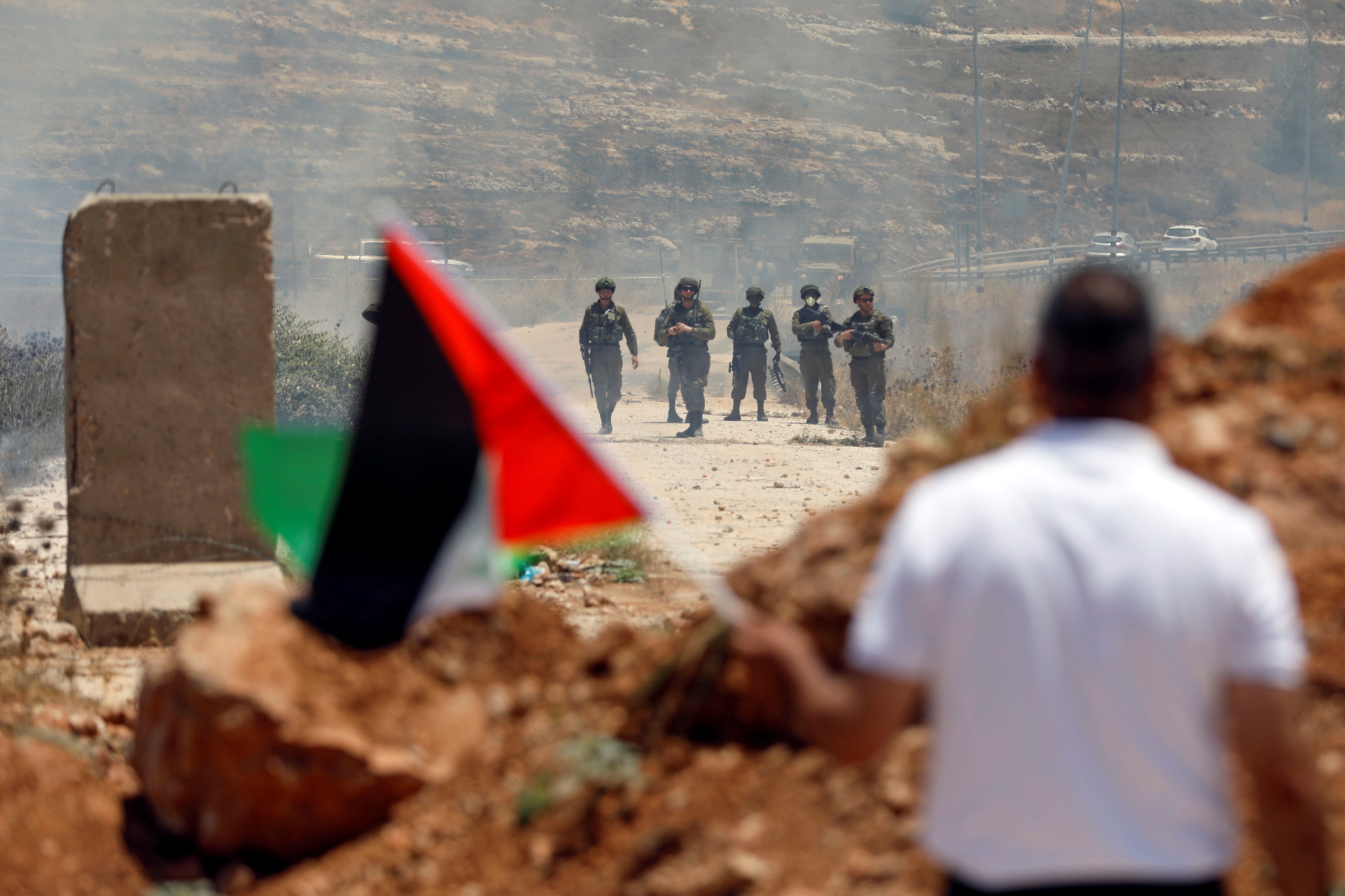  A demonstrator waves a Palestinian flag in front of Israeli forces in the Israeli-occupied West Bank on 25 June (Reuters)