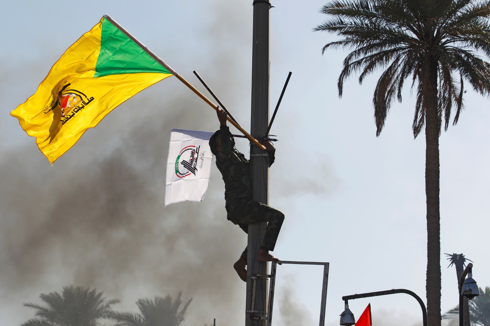 A member of Hashd al-Shaabi paramilitary forces holds a flag of Kataeb Hezbollah militia group during a protest to condemn air strikes on their bases, in Baghdad in December (Reuters)