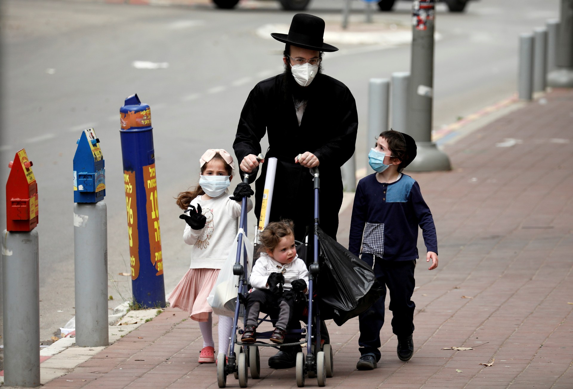 An Ultra-Orthodox Jewish family wearing masks walk on a pavement in Bnei Brak (Reuters)