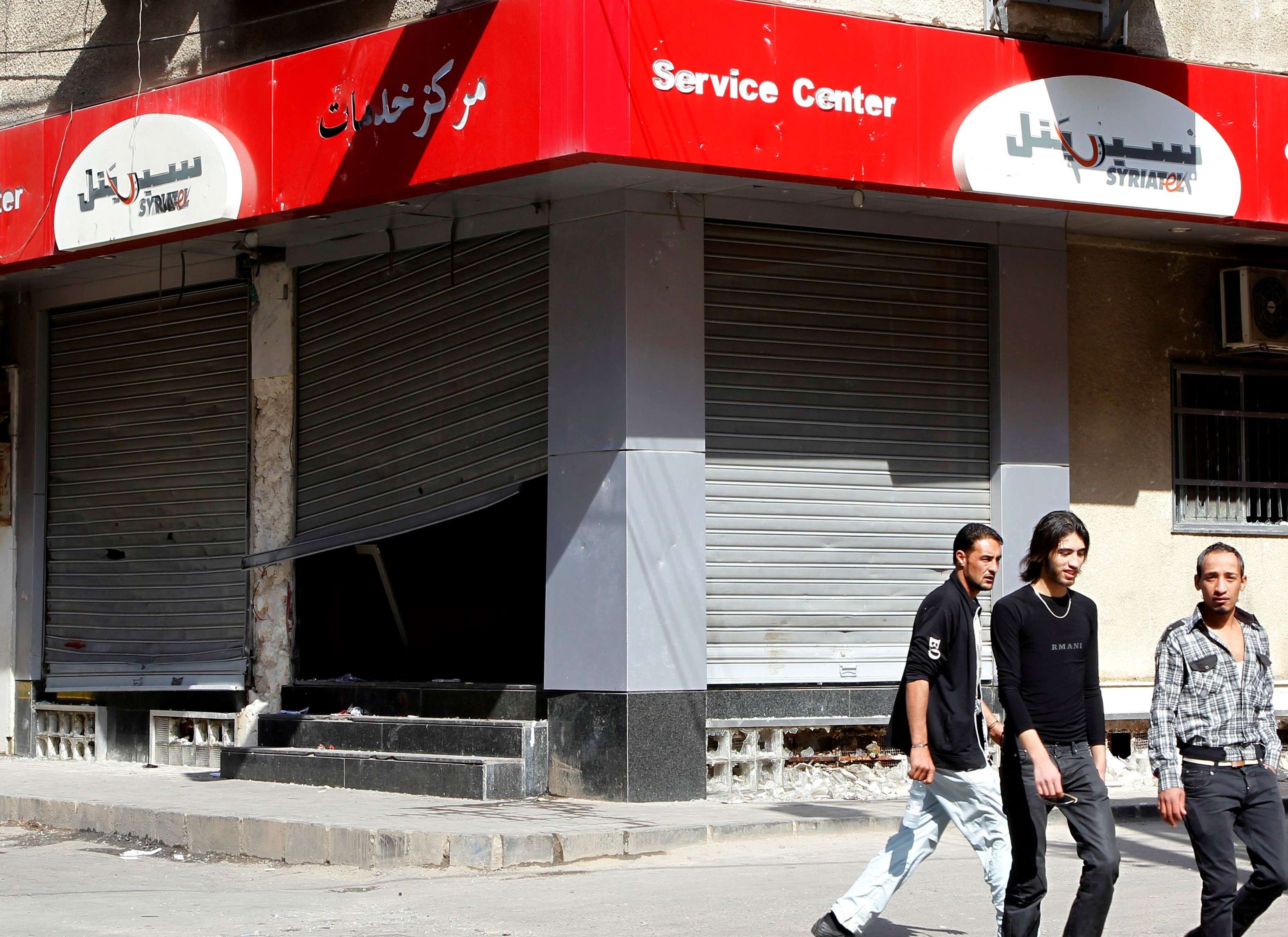 People walk past the looted premises of cellphone company Syriatel, which is owned by Rami Makhlouf, the cousin of Syria's President Bashar al-Assad, in Deraa on 21 March, 2011 (Reuters)