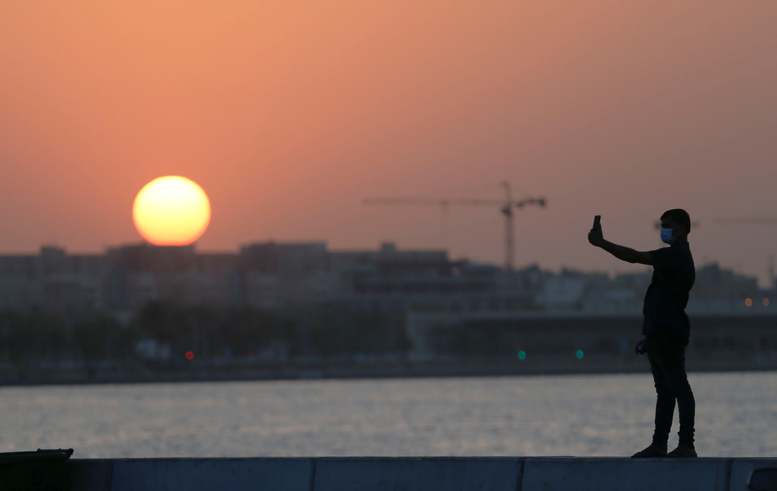 A man takes a selfie with his smart phone at sunset, during a corniche walk in the late hours of the afternoon, in Doha, Qatar, 3 September 2021 (Reuters)