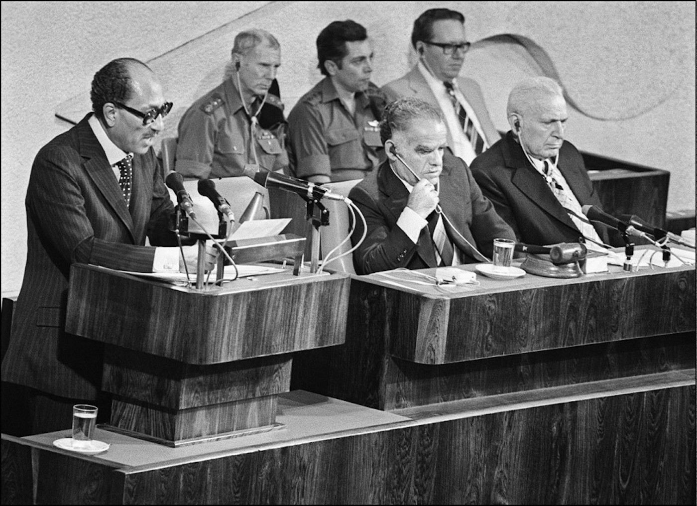 Anouar al-Sadate, en visite historique en Israël, fait un discours à la Knesset, aux côtés du ministre israélien des Affaires étrangères Yitzhak Shamir et du Premier ministre Menahem Begin, le 27 novembre 1977.  Il sera assassiné quatre ans plus tard durant une parade militaire au Caire par des membres de l’armée appartenant à l’organisation du Jihad islamique égyptien qui s’opposaient aux négociations entamées par Sadate avec Israël ainsi qu’à la vague d’arrestations qu’il avait lancée en septembre contre 