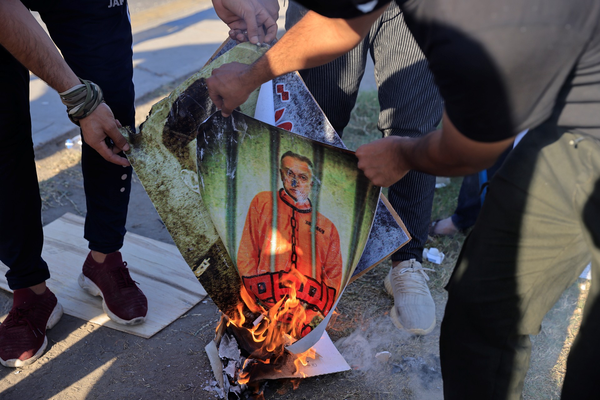 Supporters of Shia armed groups burn portraits of Prime Minister Mustafa al-Kadhemi and Iraq security officials during a protest against the election results 6 November (Reuters)