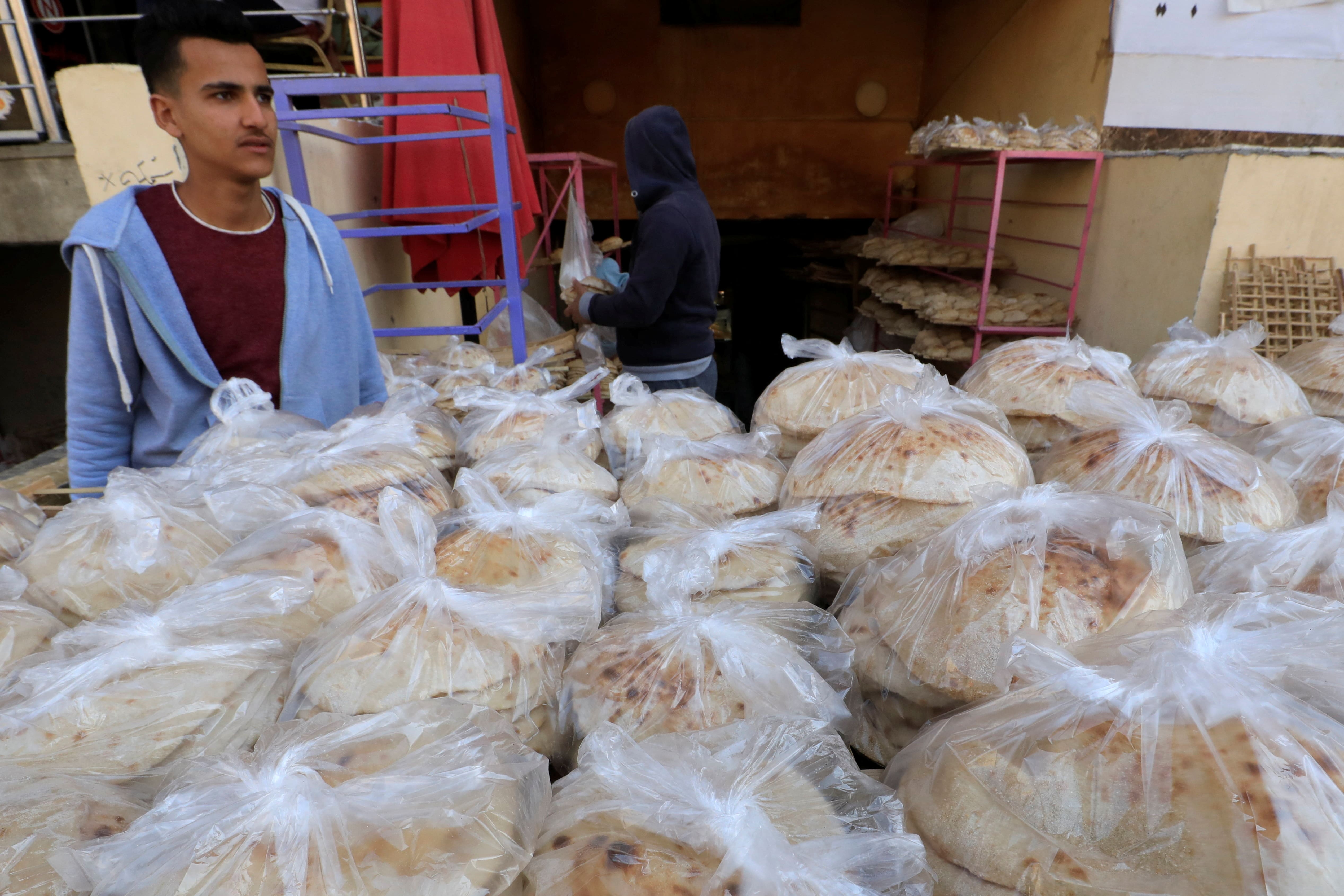 An Egyptian baker seller waits for costumers with plastic bags of bread outside a bakery in Cairo's southeastern Mokattam district in 16 March 2022 (Reuters)