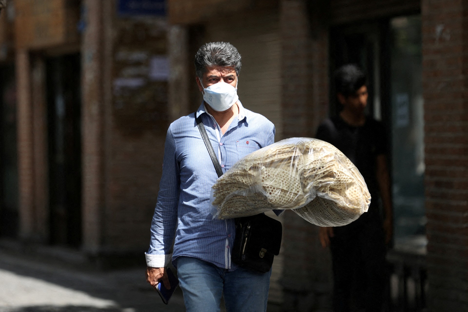 An Iranian man holds stacks of bread as he walks along a street in Tehran (Reuters)