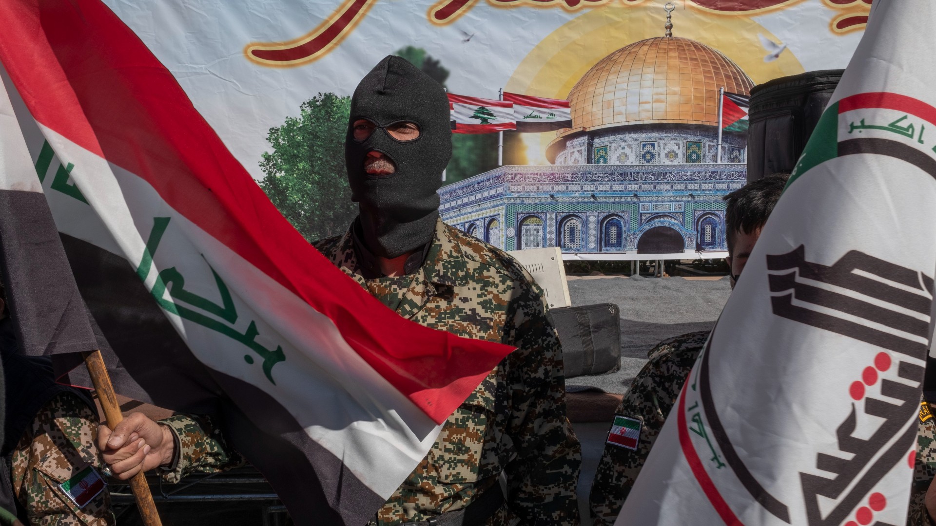 A member of the Iranian Basij paramilitary force holds an Iraqi flag while standing guard next to a flag of the Hashd al-Shaabi Iraqi paramilitaries during a rally in Tehran in April (Reuters)